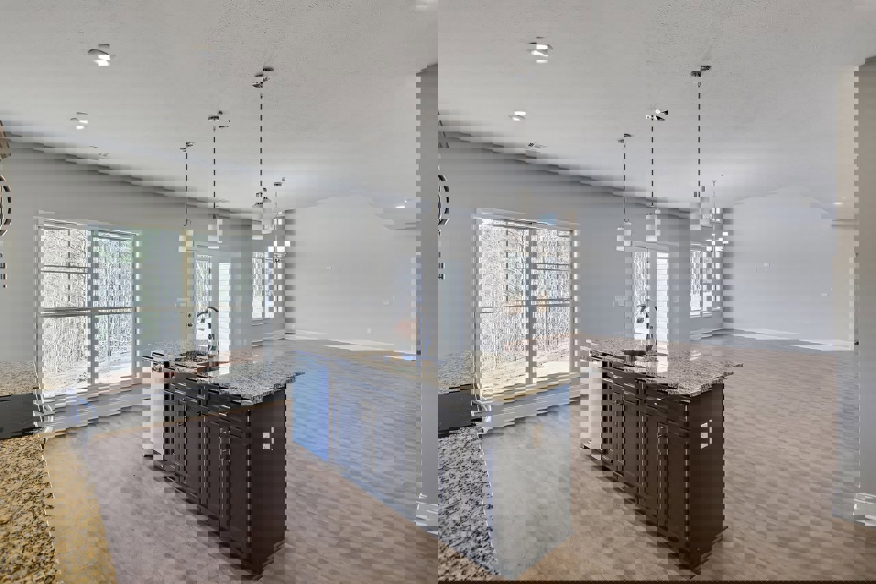 Kitchen with wood flooring, granite island countertop, stainless steel sink and faucet, white cabinetry, large window overlooking trees