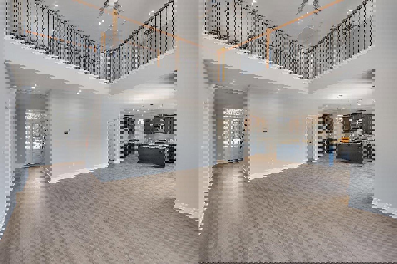 Spacious open-concept living area featuring hardwood floors, black kitchen island with marble countertop, white door with glass panes, metal vented bar, ceiling fan, and staircase