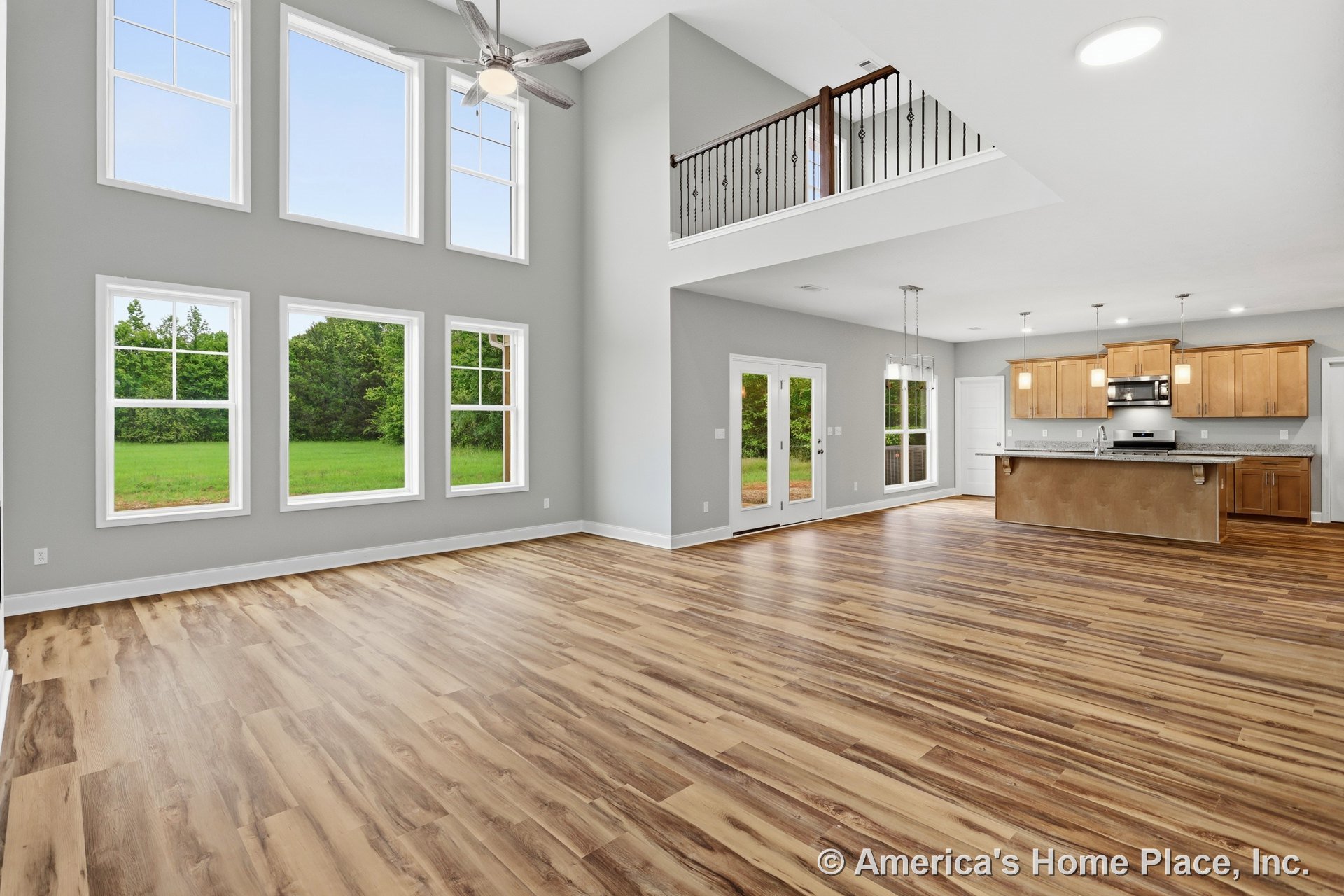 Double-height ceiling living area with wall of large windows, open floor plan connecting kitchen with wood cabinetry and granite countertops, wood-look plank flooring, pendant