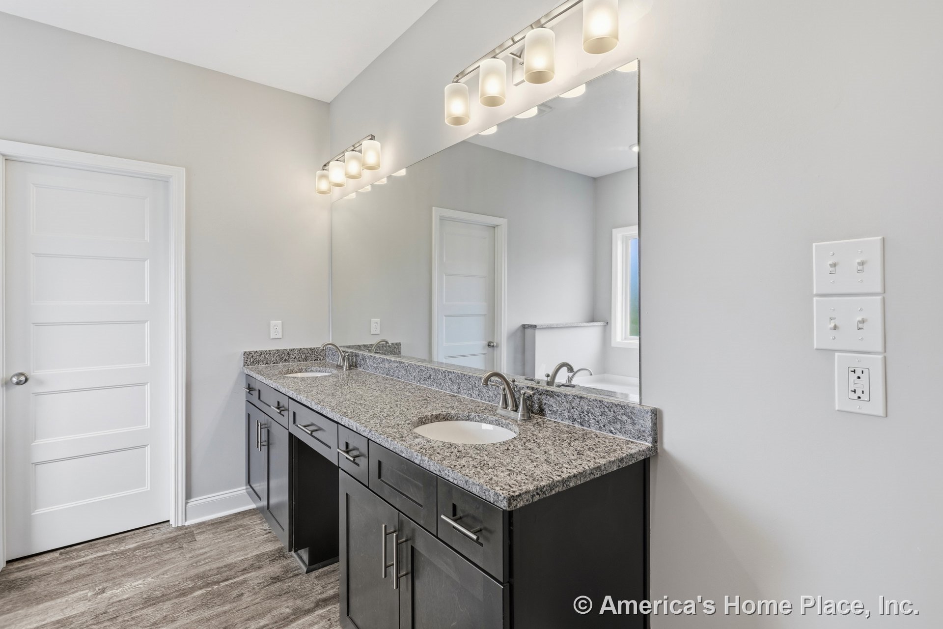 Double vanity with dark wood cabinetry and granite countertop, two undermount sinks, expansive wall mirror, modern vanity lighting, wood-look flooring, neutral wall color, white