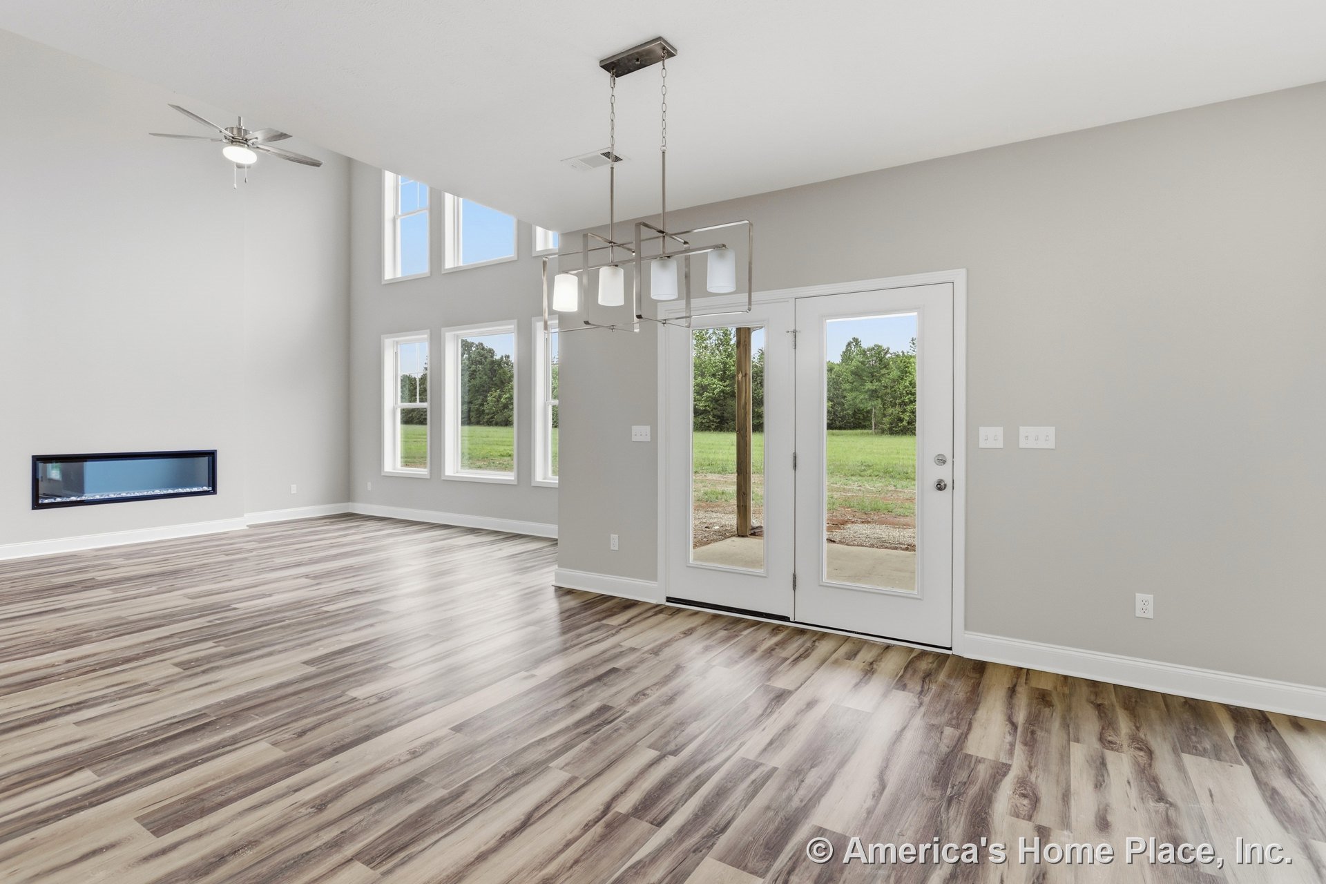 Double-height living room with expansive windows, modern linear wall fireplace, wood-look plank flooring, glass patio doors, neutral walls, and contemporary chandelier.
