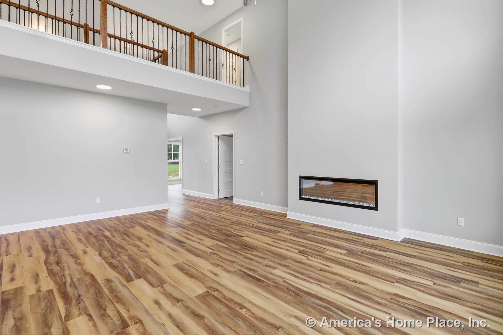 Modern living room with linear wall fireplace, wood-look plank flooring, double-height ceiling, white trim and baseboards, upper-level balcony with iron railing, recessed lighting