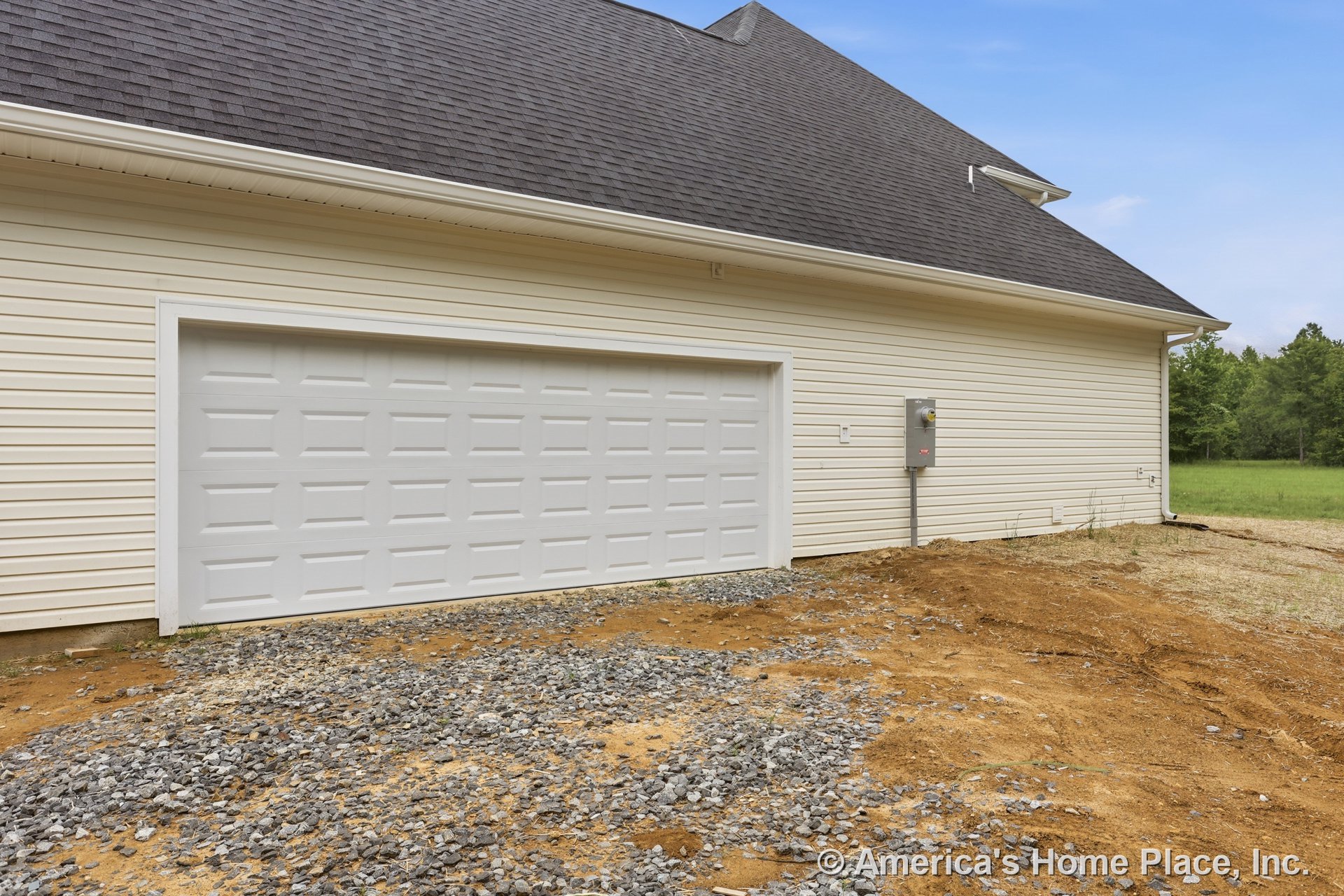 Double garage door with light-colored vinyl siding, shingle roof, gravel driveway, white trim, and visible electrical panel on exterior wall.