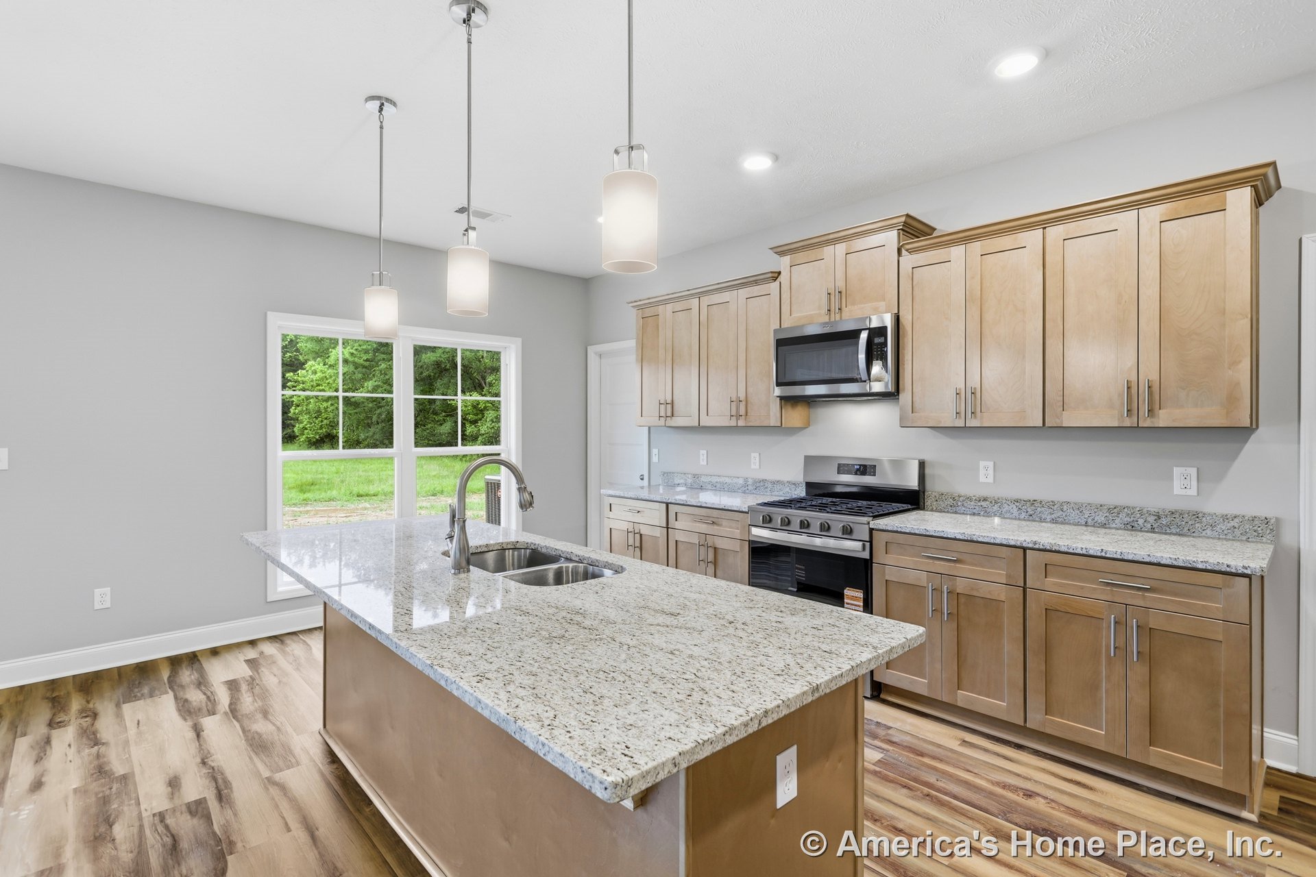 Spacious kitchen with large island featuring sink, granite countertops, light wood cabinetry, stainless steel gas range and built-in microwave, pendant lighting fixtures, wide