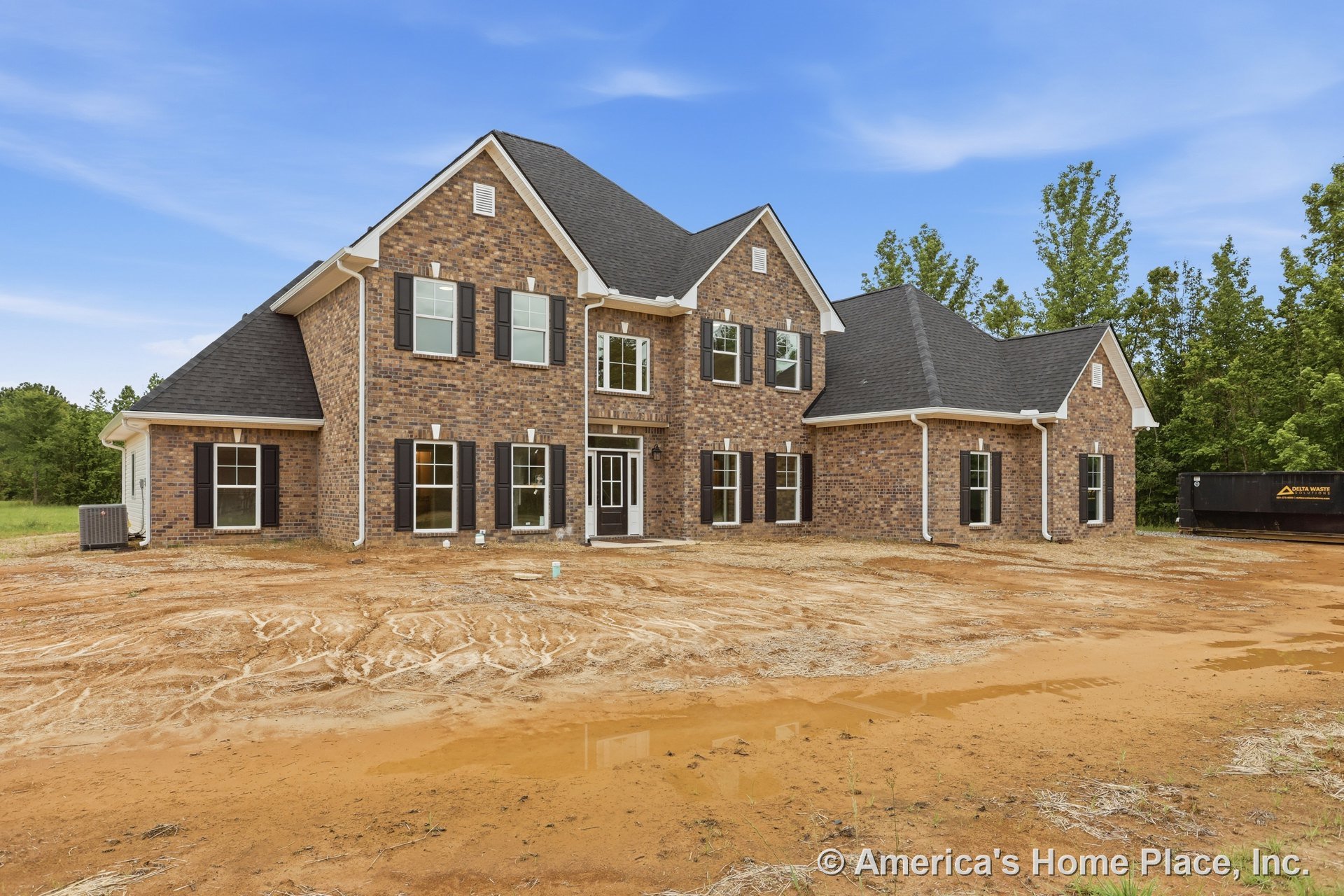Two-story brick facade with black shutters, white trim accents, multiple double-hung windows, covered front entry, and dark shingle roof.