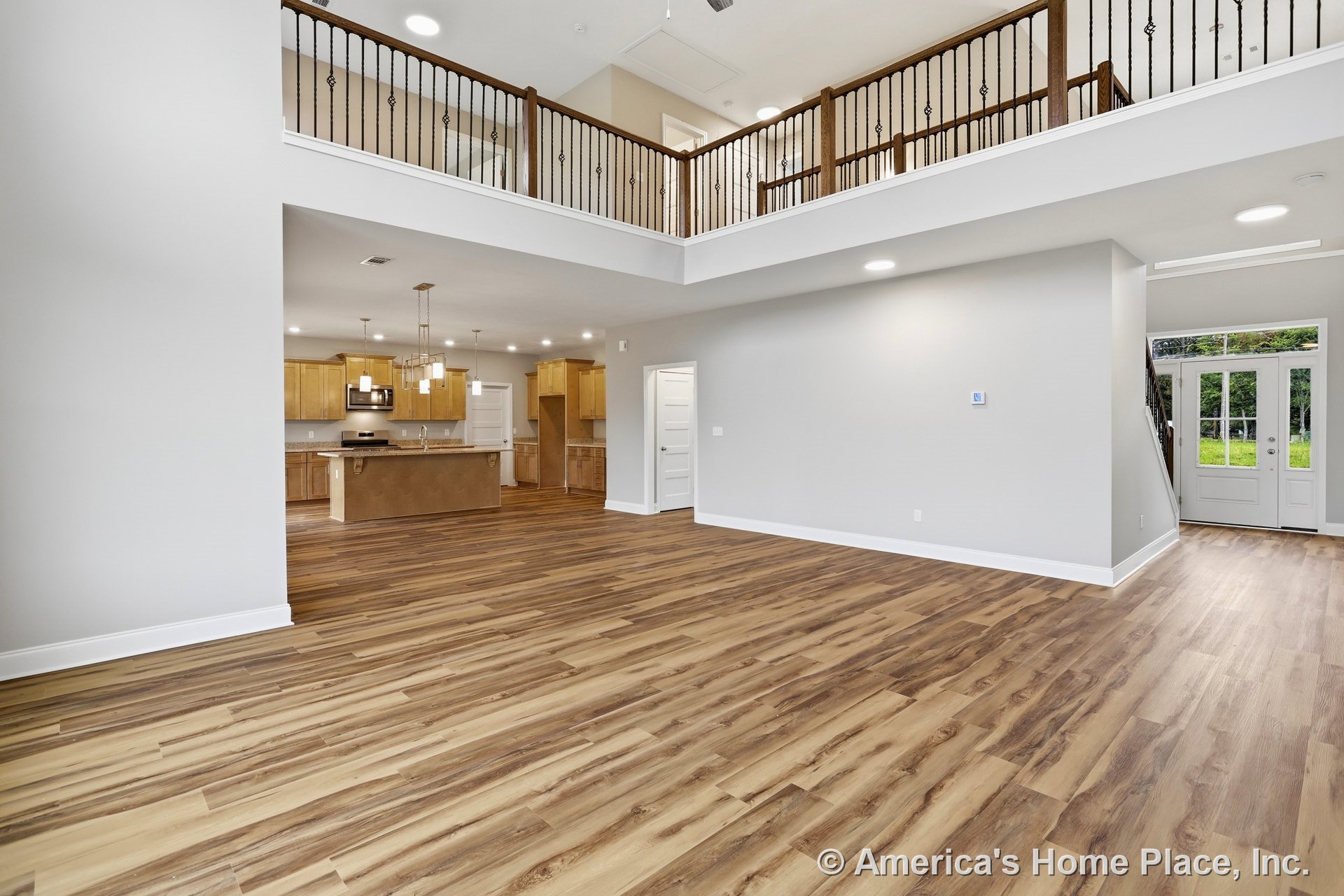Open living area with wood-look plank flooring, soaring two-story ceiling with recessed lighting, iron and wood balcony railing, double glass exterior doors topped by a transom