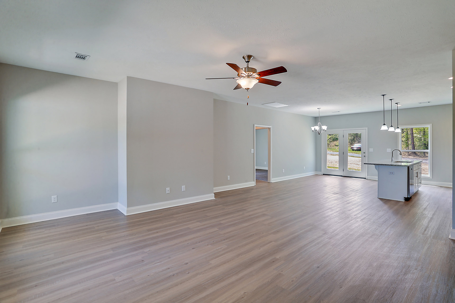 Open concept room with wood flooring, ceiling fan with light fixture, kitchen island featuring stainless steel dishwasher, and an open door leading to another space