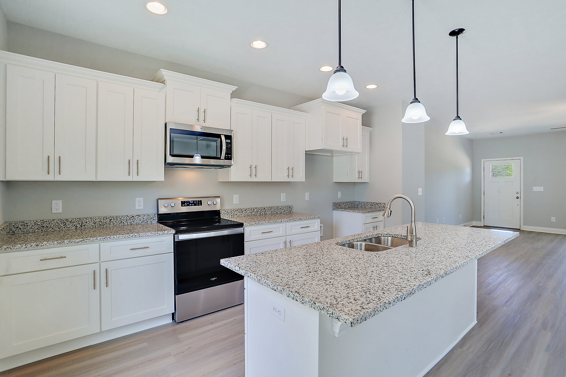 Granite countertops, white shaker cabinets, stainless steel microwave, undermount sink with chrome faucet, pendant light fixture, white door with glass window