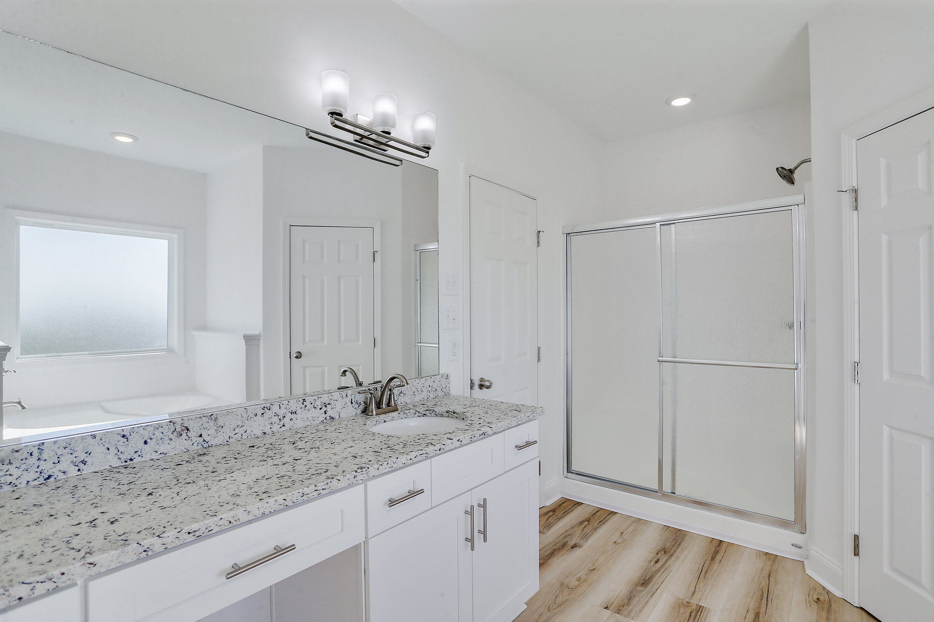 Bathroom featuring marble countertop with undermount sink, glass shower enclosure, silver hardware, frosted window, and white cabinetry