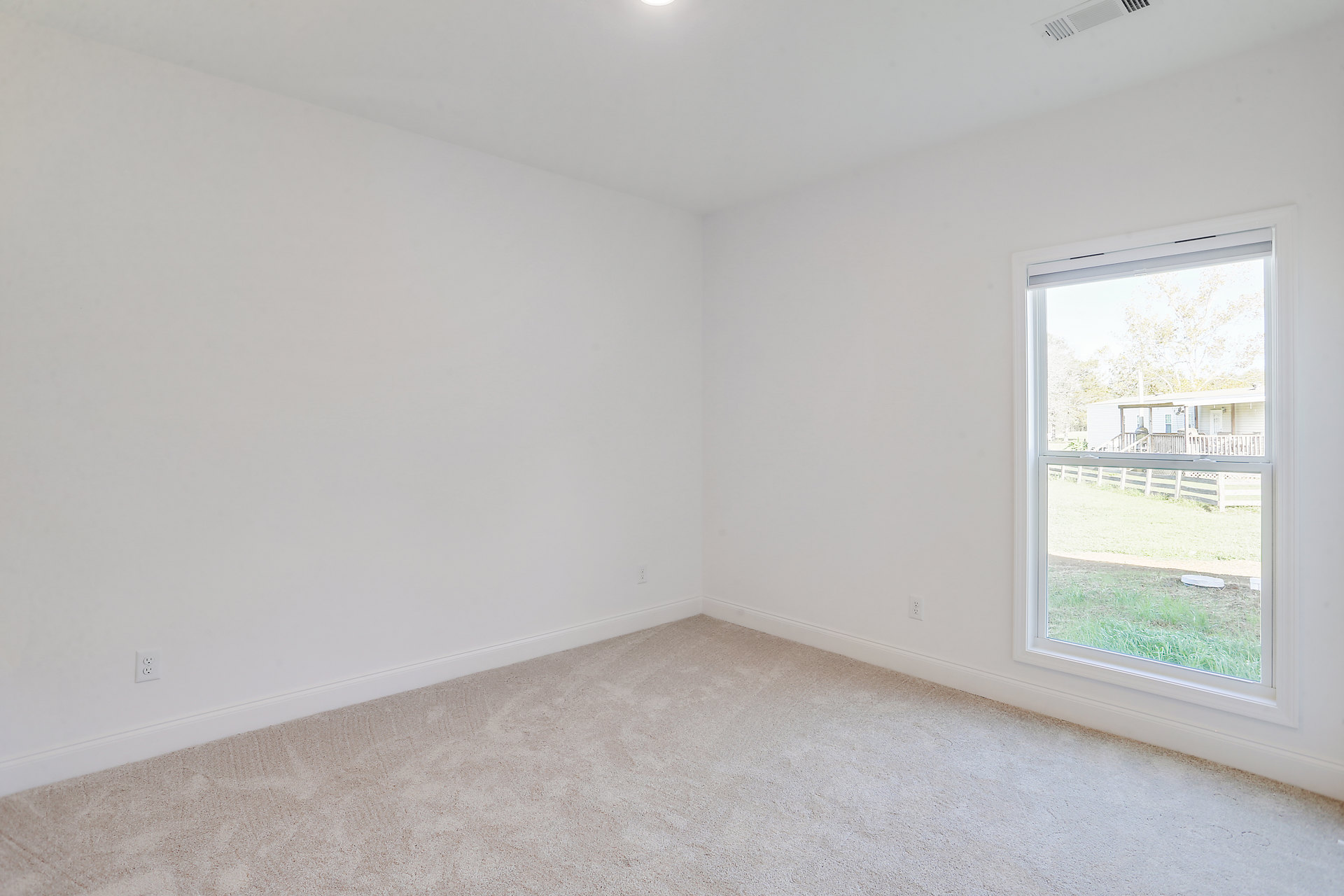 Bright room with white carpet, large window overlooking fenced yard with green grass, smooth plaster walls, and minimal decor