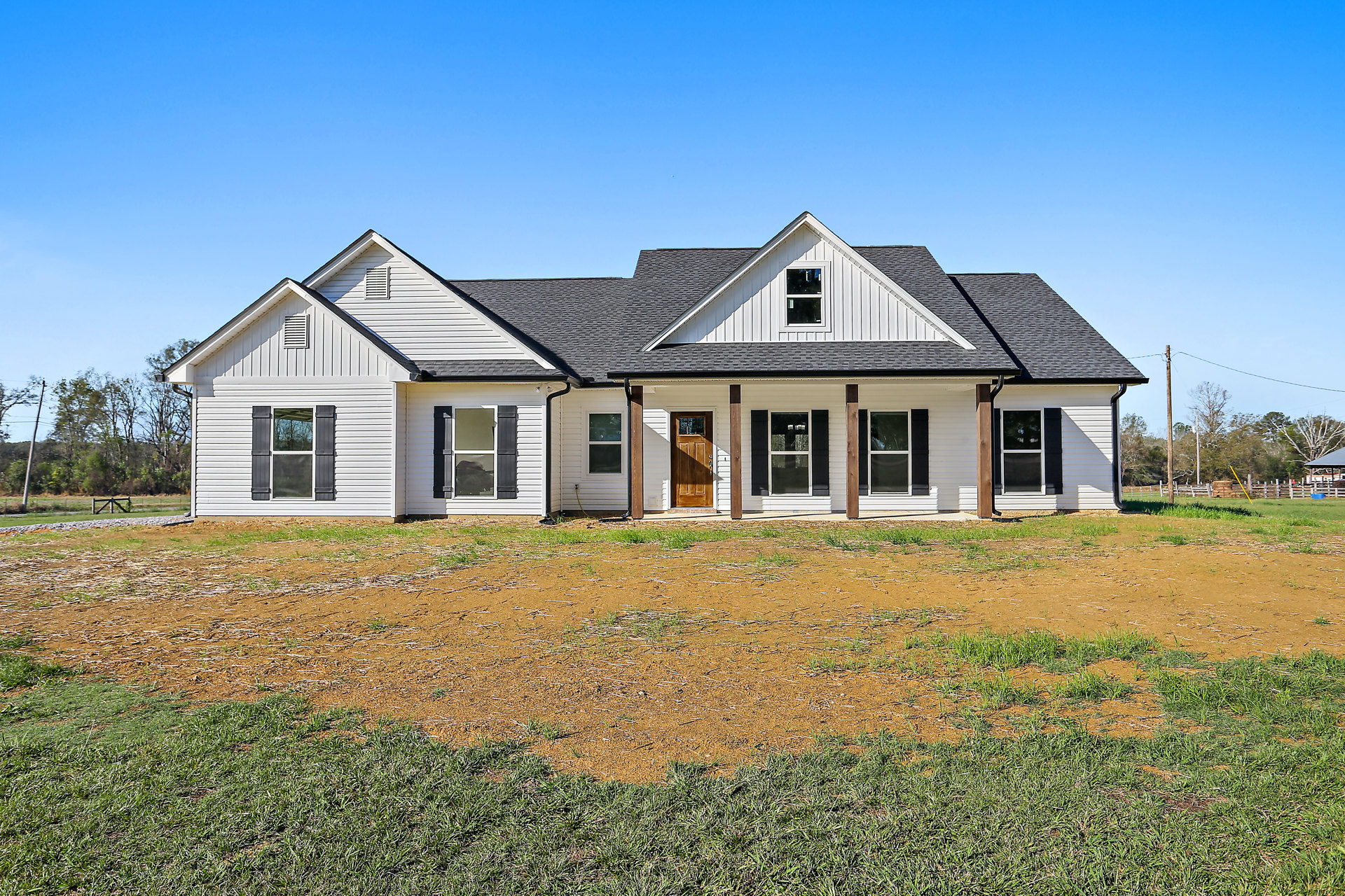 White farmhouse with black roof, wooden front door with glass panel, white-framed windows, green lawn, and blue sky