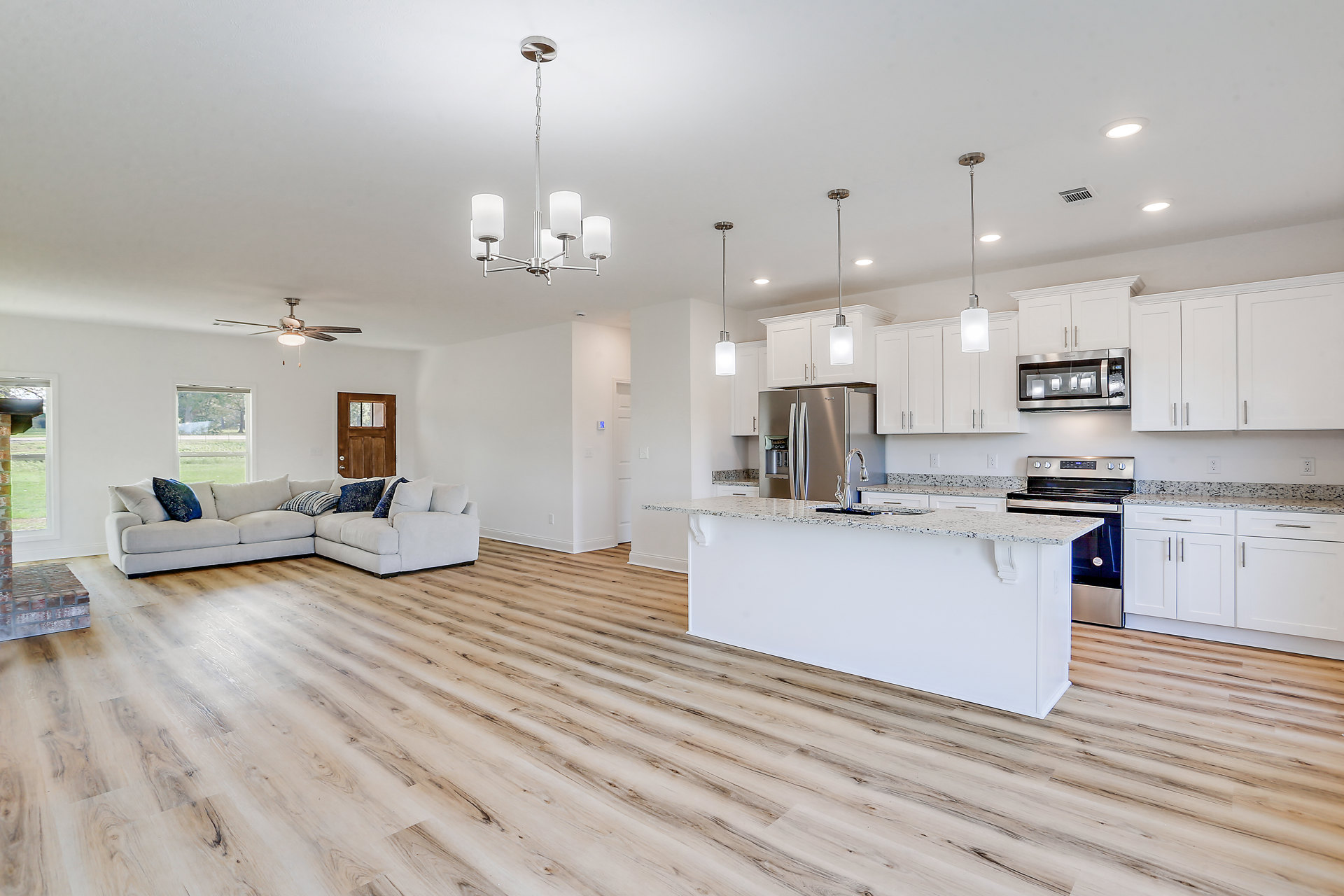 Open-concept kitchen and living room featuring wood flooring, stainless steel refrigerator, kitchen counter with sink, cabinetry, couch with pillows, wooden door with window, and