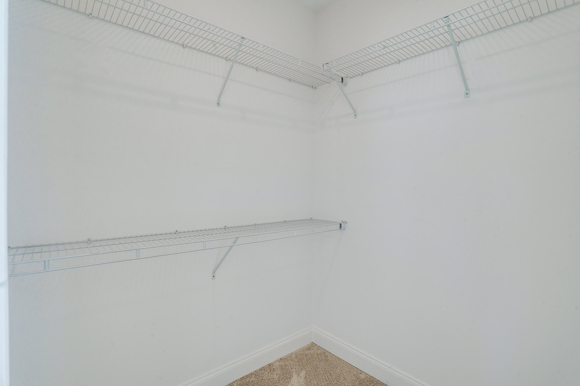 White built-in shelves on a plaster wall with a metal hanging rod above a light tile floor in a minimalist room.