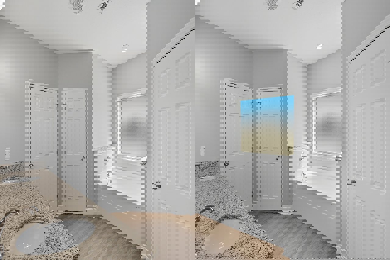 Bathroom with white speckled sink, freestanding tub, frosted glass window, white door with silver handle, light cabinetry, and neutral tile flooring