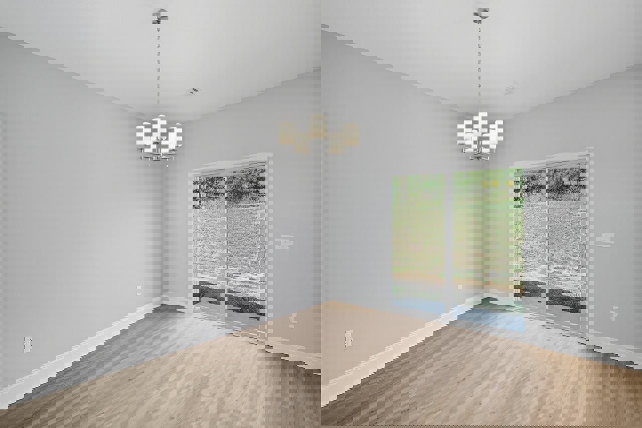 Wood flooring in a room with a sliding glass door opening to a grassy yard, white chandelier hanging from the ceiling with visible chain, plaster walls, and crown molding.