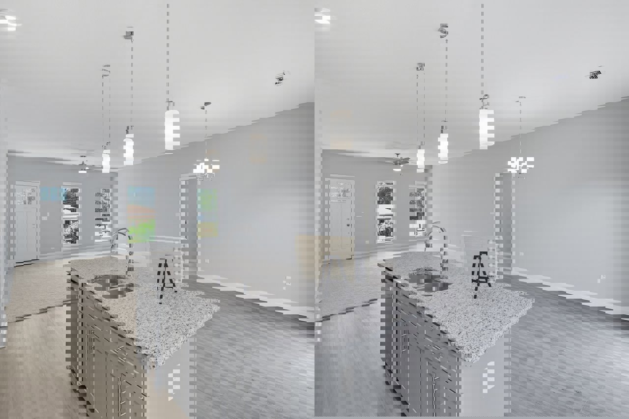 Open-concept kitchen featuring a large island with white quartz countertop, stainless steel sink, blue and white towel draped over the edge, white cabinetry, tile backsplash, black