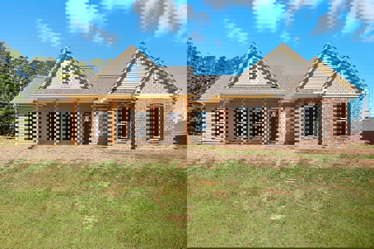 Brick exterior home with white-framed windows, brown front door, and manicured green lawn under a partly cloudy sky