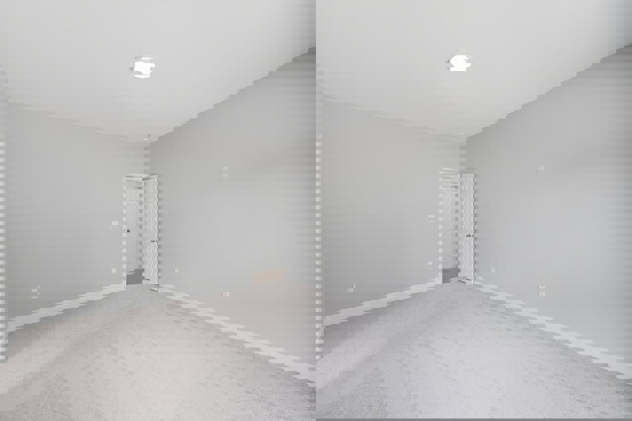 White carpeted room with white plaster walls, white ceiling light fixture, and a white door featuring a silver handle.