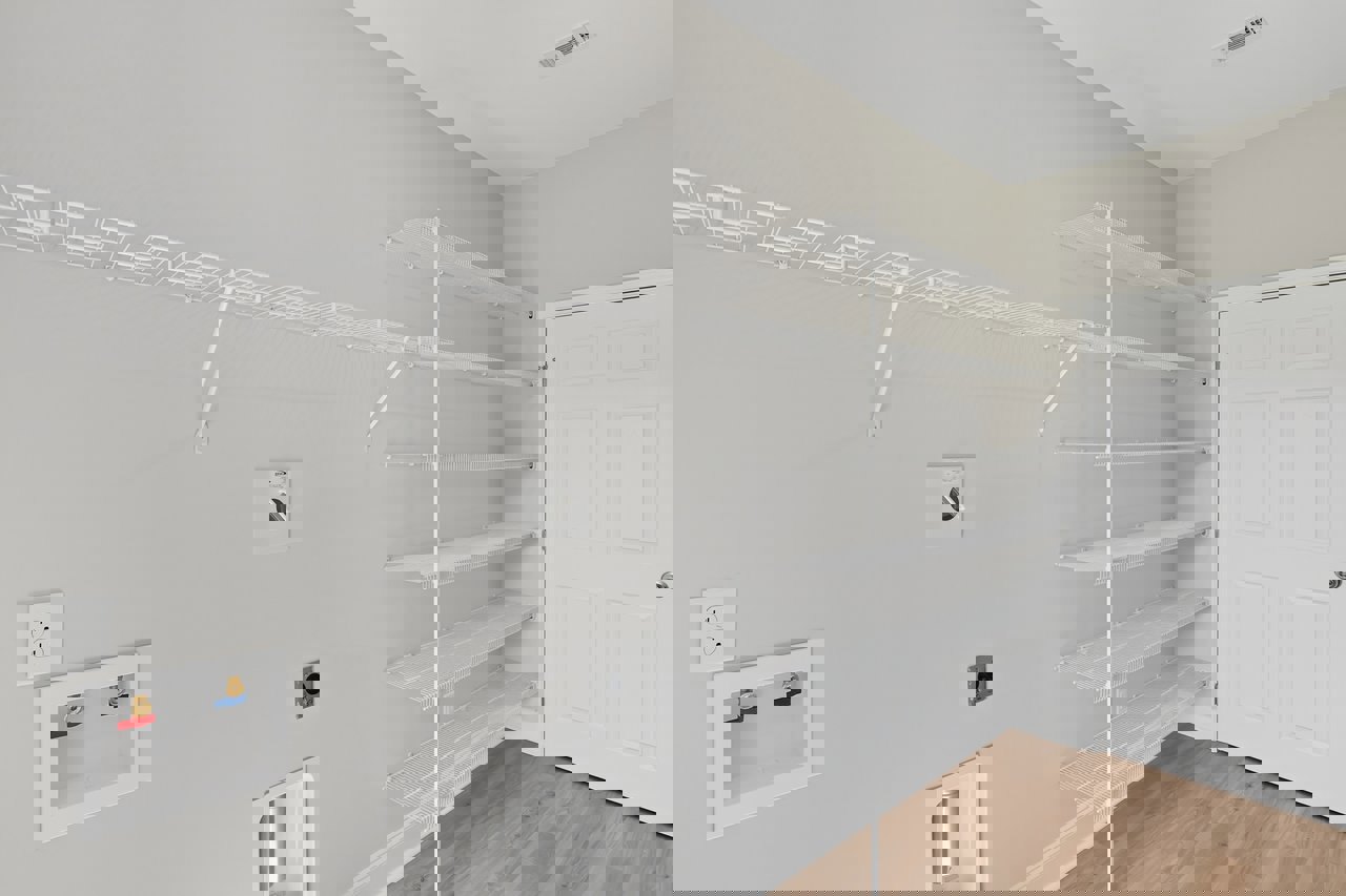 Built-in white shelving unit beside a white door with silver knob, white utility box featuring red and blue valves, electrical outlet, and light-colored flooring in a