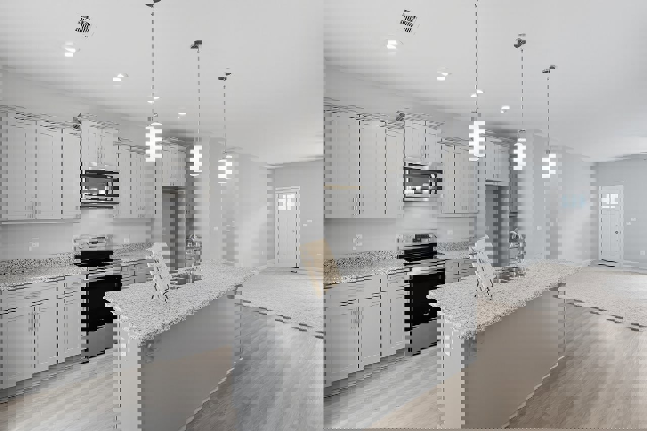 Marble kitchen island with built-in stove, white cabinetry, stainless steel sink, pendant lights above, hardwood flooring, and a white door with glass window.