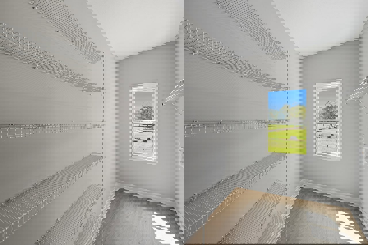 White built-in shelves on a plaster wall beside a large window overlooking a field and trees, with sunlight casting shadows on the smooth surfaces.