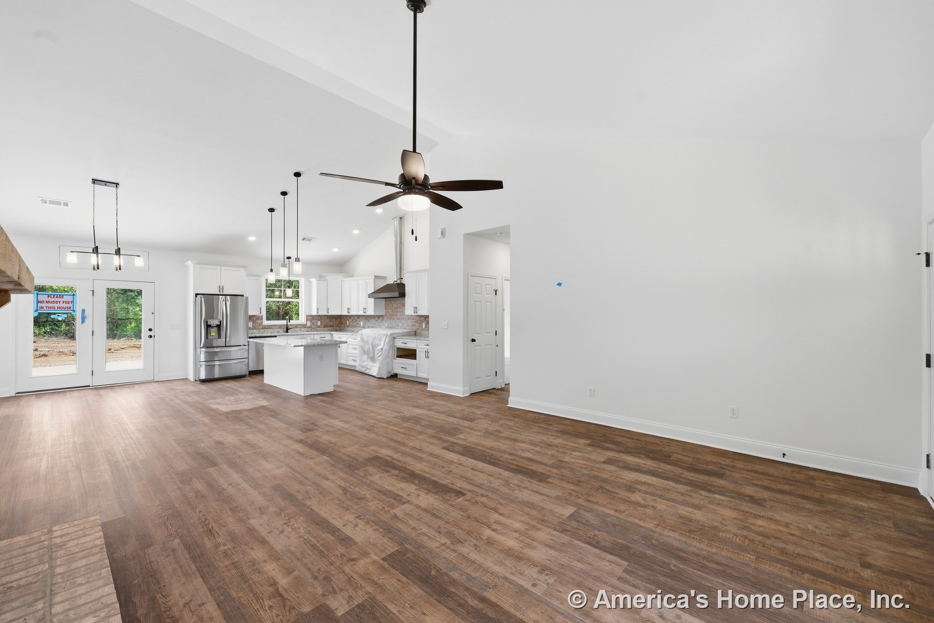 Open kitchen and living area with vaulted ceiling, ceiling fan, white shaker cabinets, central island with pendant lighting, stainless steel appliances, wood-look plank flooring