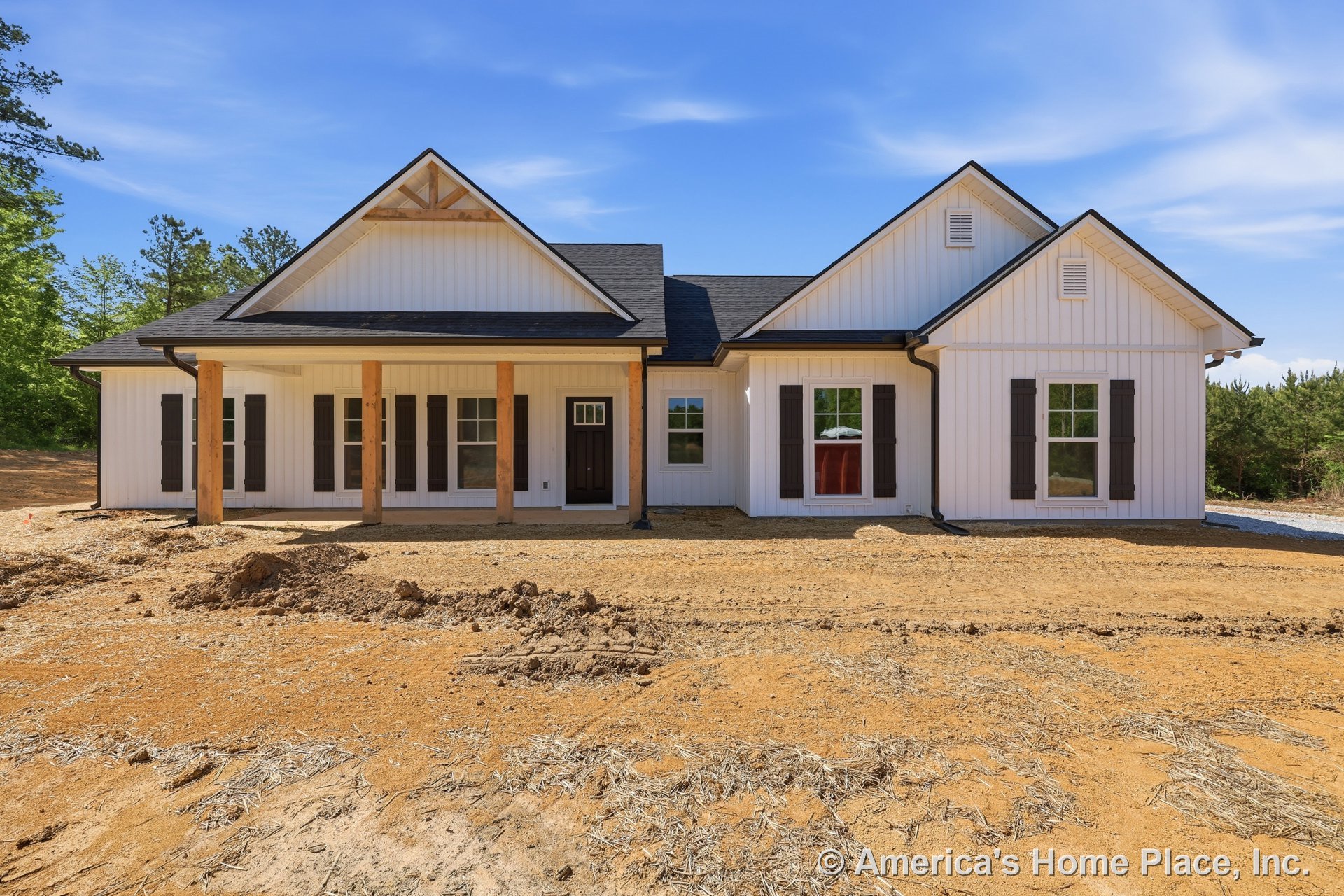 White vertical board and batten siding with black window shutters, covered front porch supported by wood columns, gable roof featuring exposed truss, and dark front door with