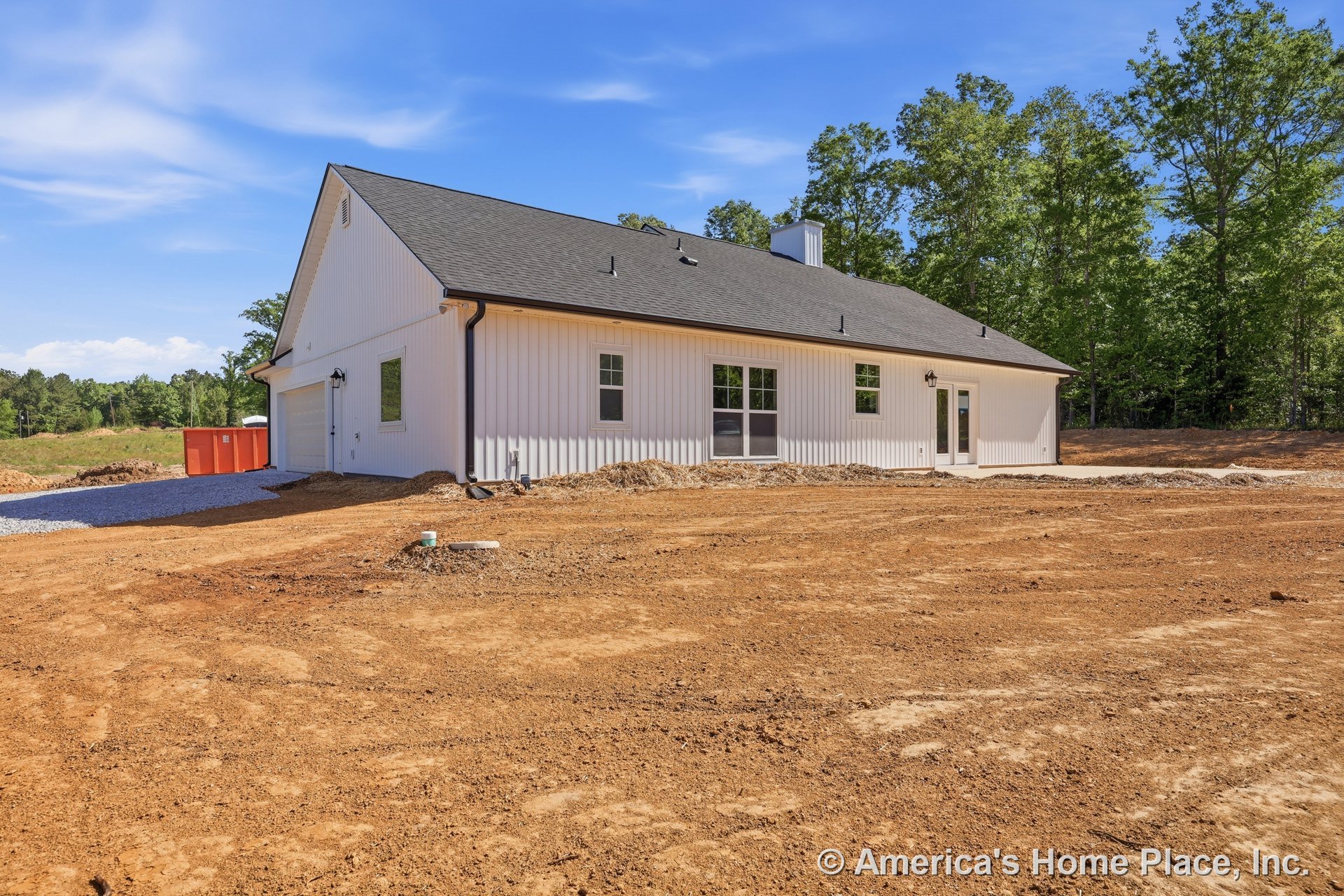 Single-story exterior with white vertical siding, dark shingle roof, multiple windows, glass-paneled exterior door, black gutters, gravel driveway, and outdoor lighting fixtures.