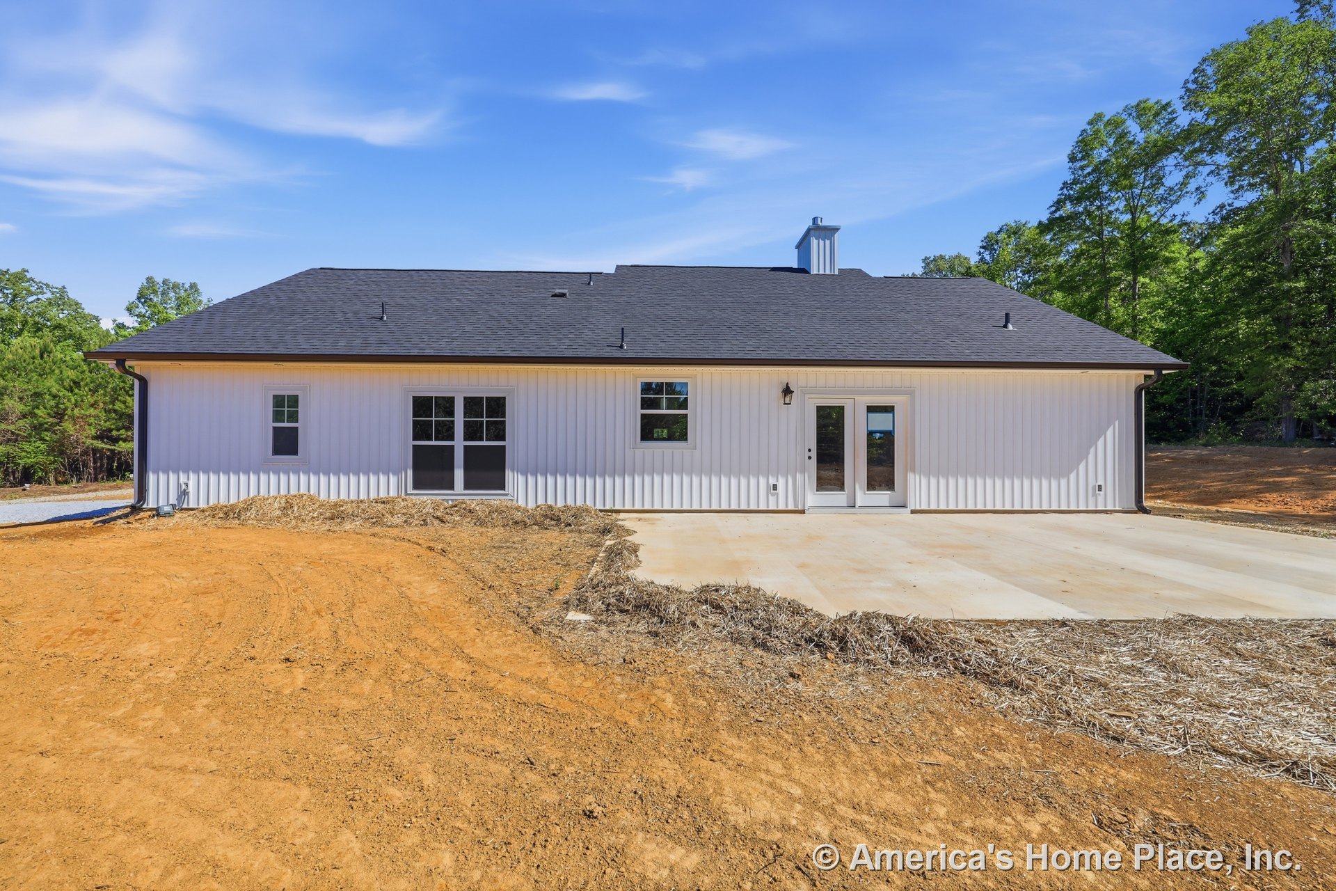 White vertical metal siding exterior with black shingle roof, concrete patio, double glass doors, multiple grid windows, and outdoor wall light fixture on a single-story modern