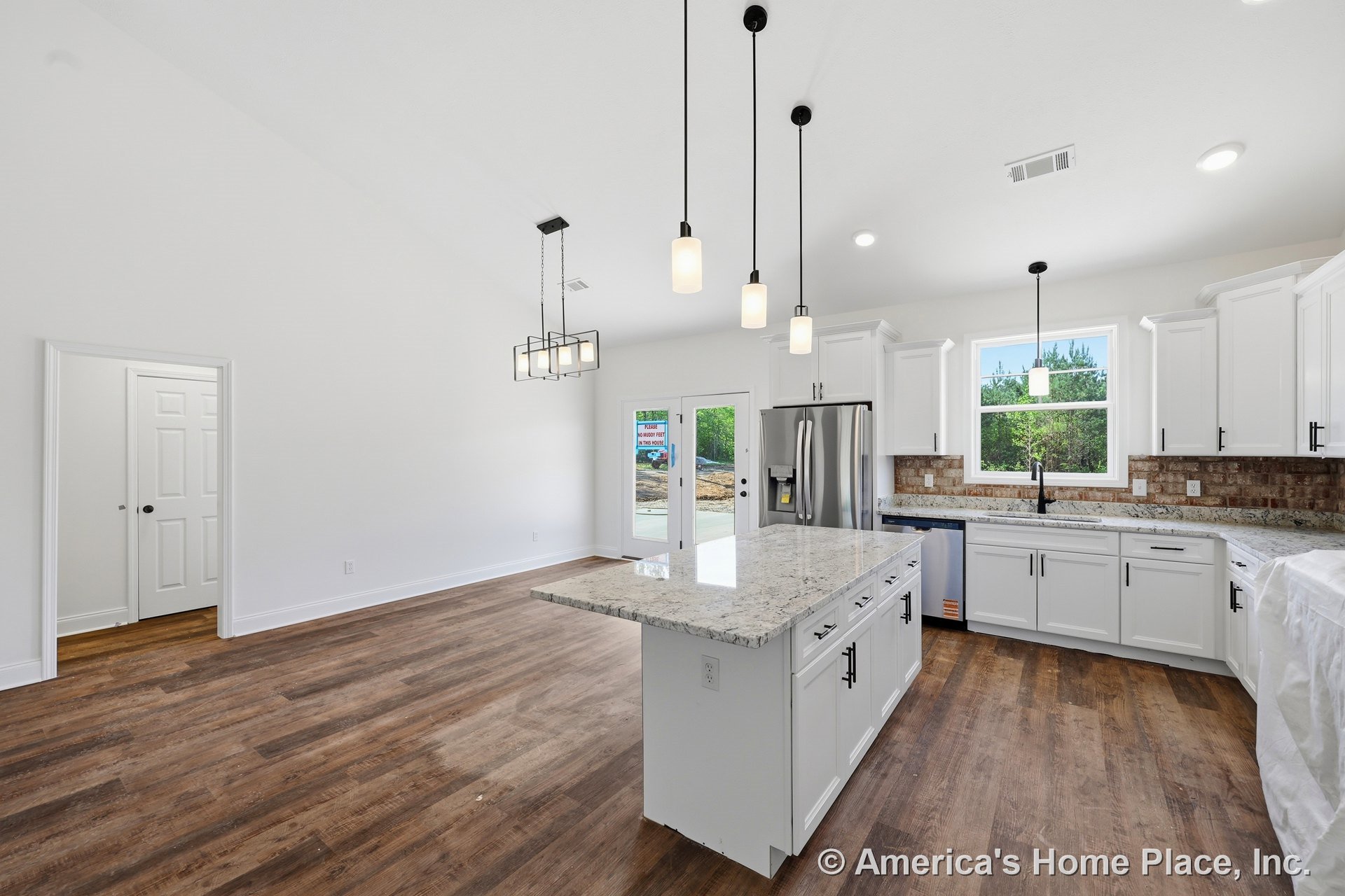 White shaker kitchen cabinets with granite island, brick tile backsplash, stainless steel refrigerator and dishwasher, wood-look flooring, modern pendant lighting, open layout
