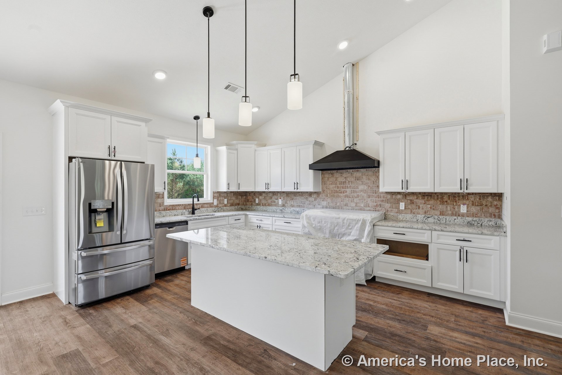 White shaker cabinets and built-in cabinetry surround a center island with granite countertop; brick tile backsplash, stainless steel refrigerator, range hood, pendant lighting