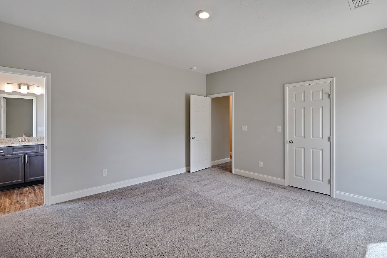 White paneled doors with silver knobs, light grey carpeted floor, white walls, and smooth ceiling in a residential interior.