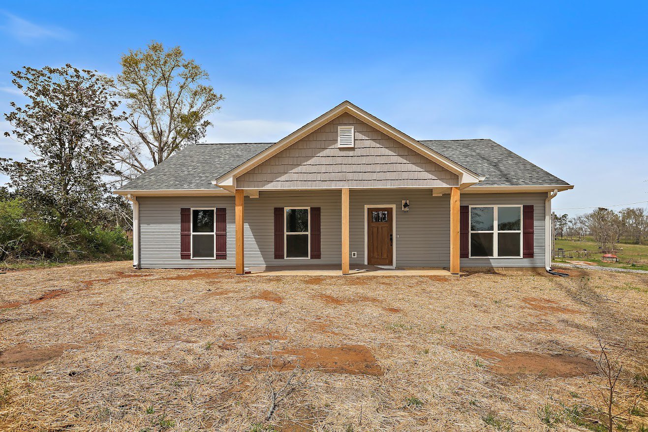 Two-story home with white siding, wooden front door with glass panel, covered porch, white-framed windows, and brown dirt yard in front