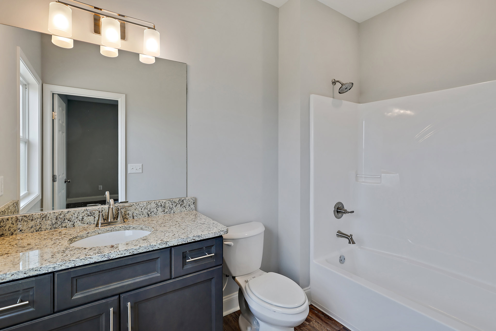 Bathroom with white tile floor, white toilet, white bathtub with chrome faucet, light wood vanity with sink and cabinets, wall-mounted mirror, and overhead light fixture with white