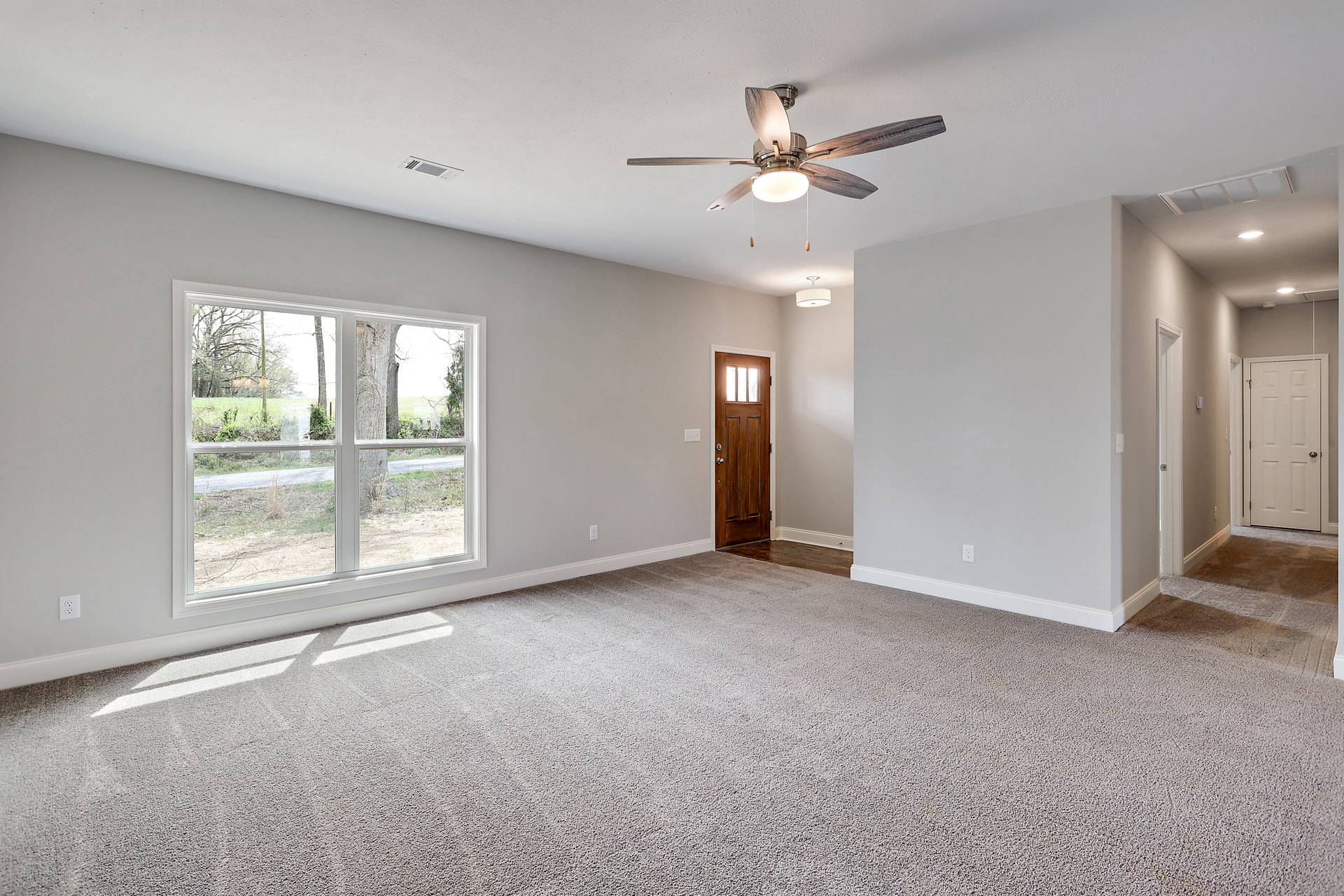 Carpeted room with white walls, ceiling fan with light, white door with silver knob, window overlooking trees