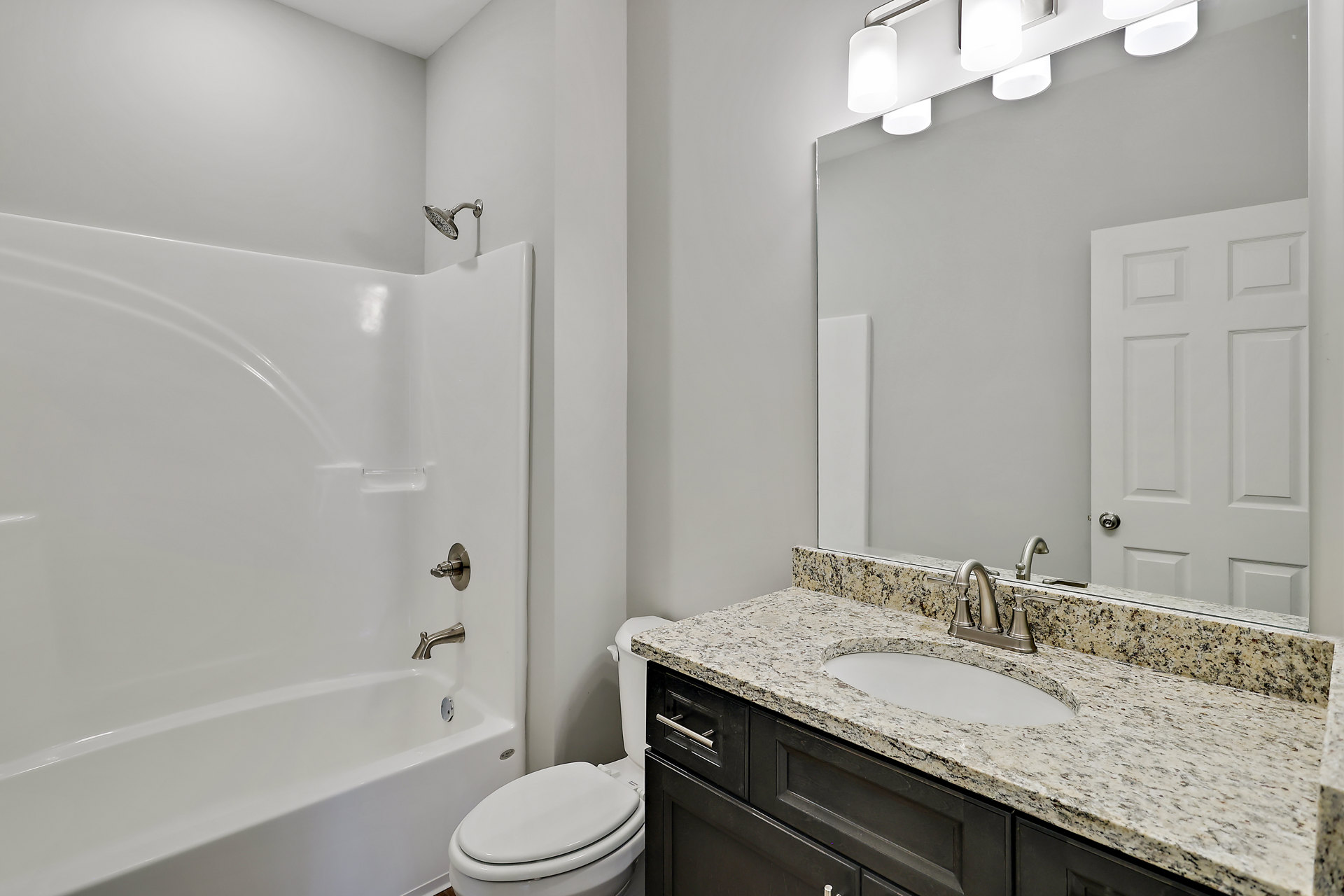 Modern bathroom featuring white porcelain sink with chrome faucet, wall-mounted shower head, white toilet with lid open, and a bathtub with silver fixtures; light-colored tile