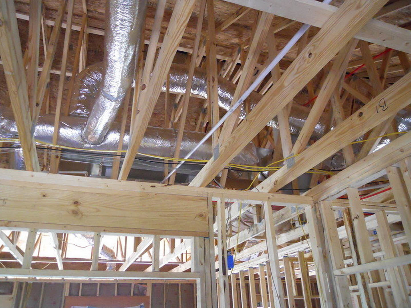 Exposed wood framing and beams with visible metal ductwork and pipes in a house under construction