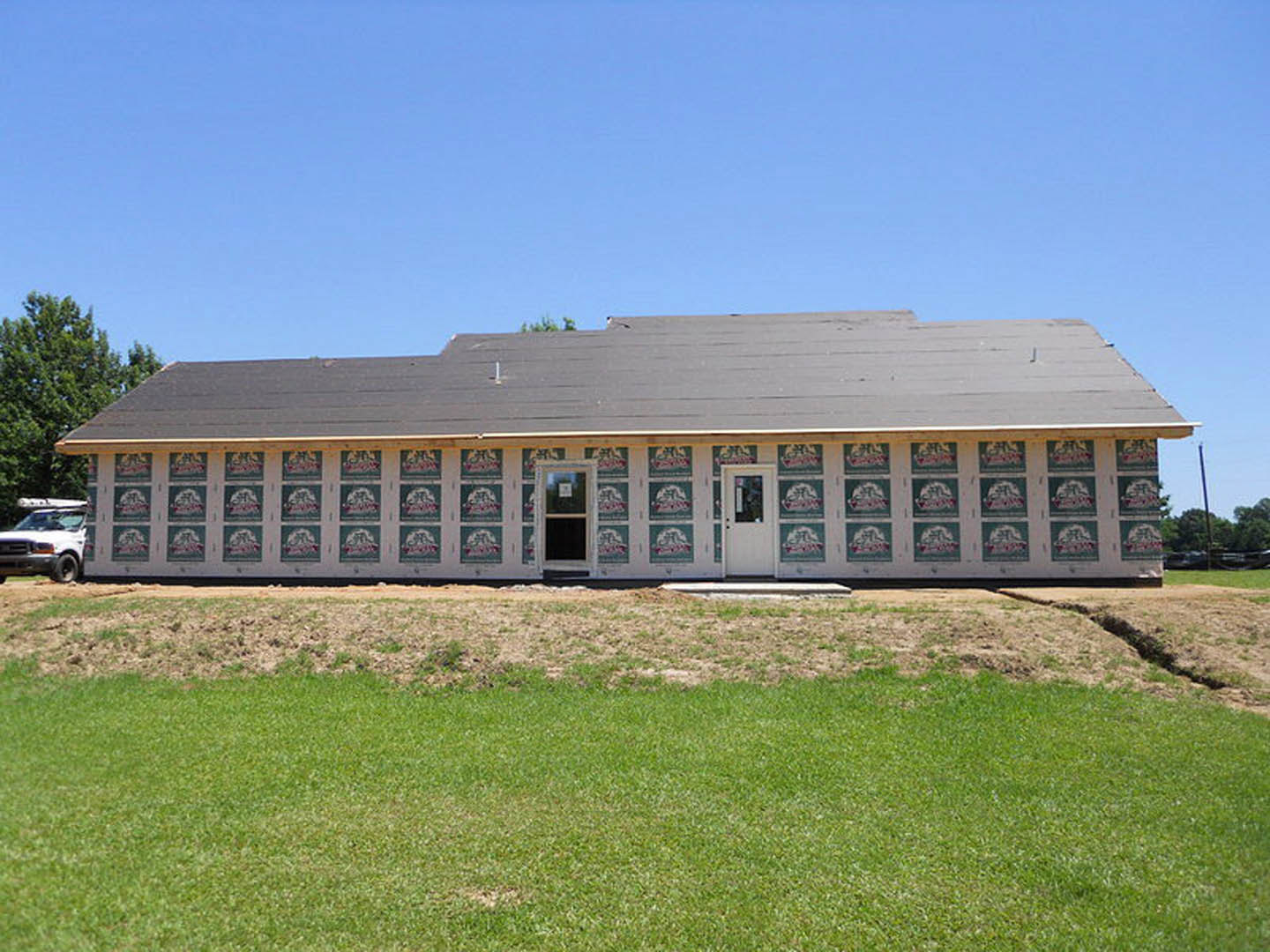Modern two-story house with large windows, white front door, manicured lawn, and mature trees under a clear sky