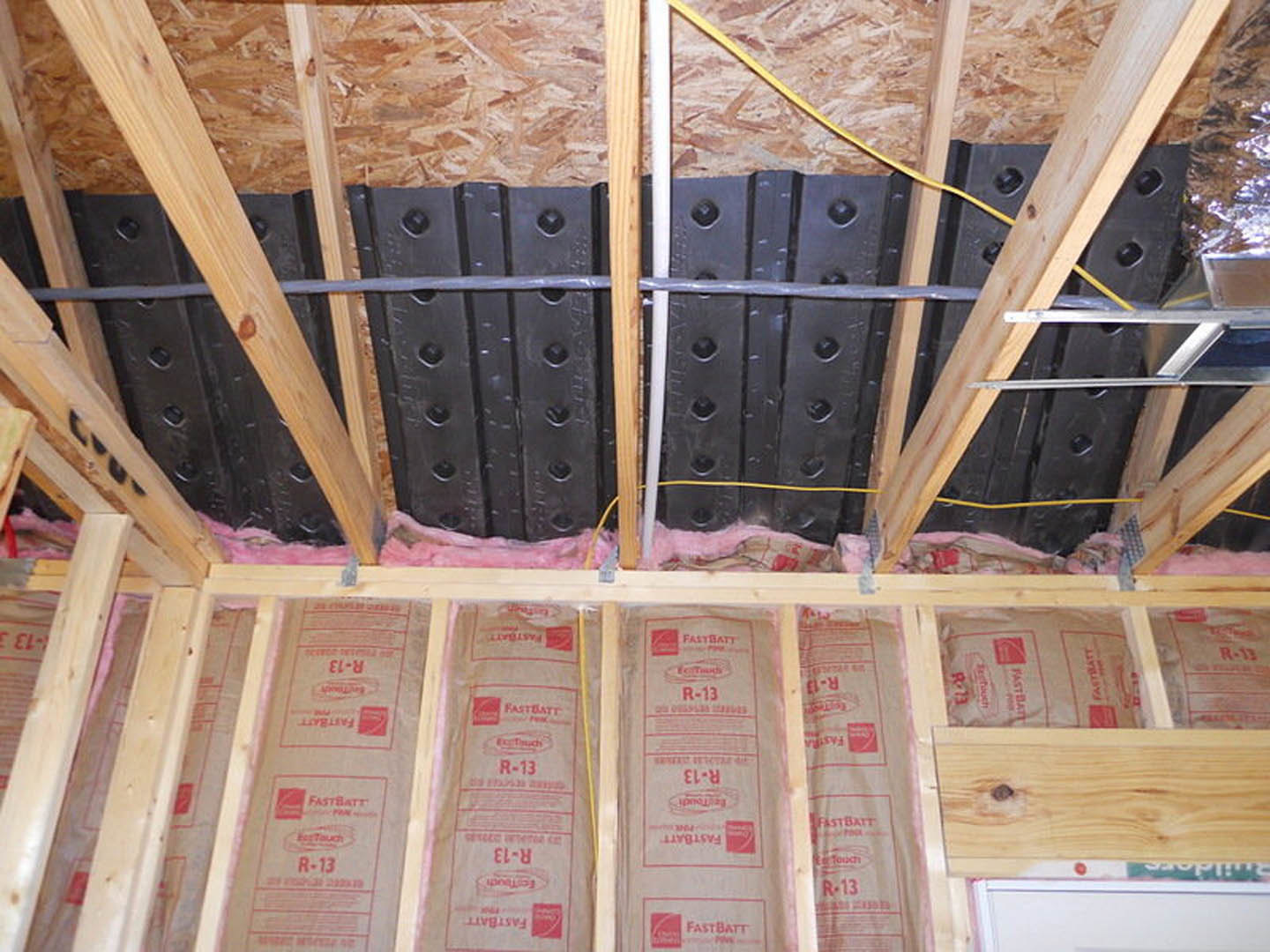 Wooden roof beams with thick insulation panels, black perforated metal plates, and screws securing materials in a residential interior construction.