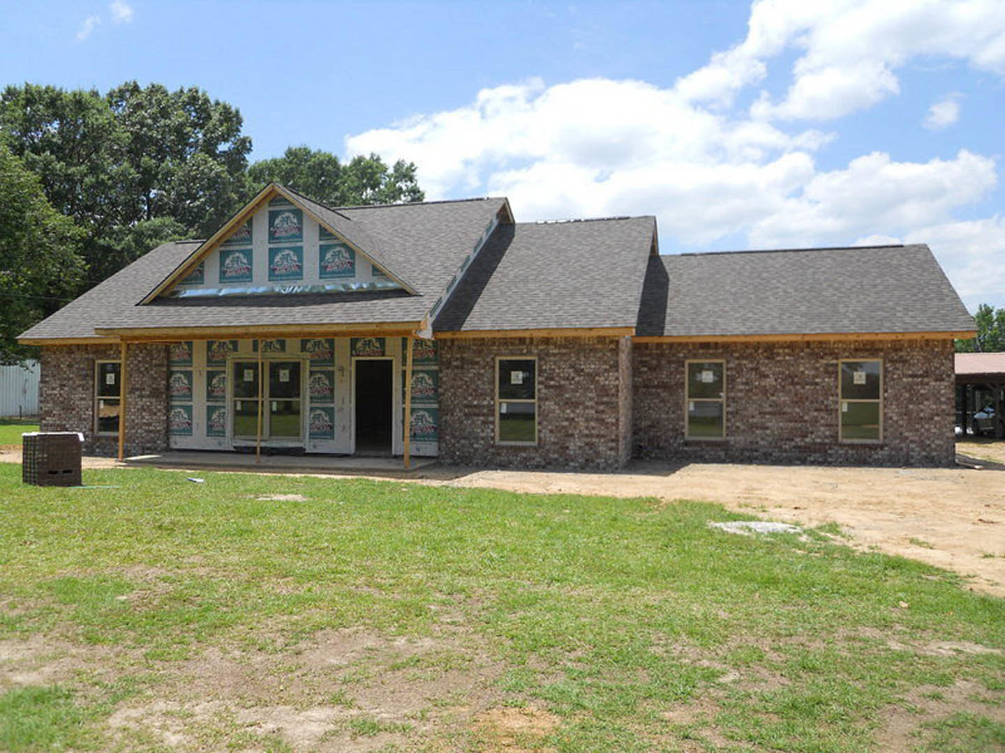 Red brick house with white-framed windows, open front door, and green lawn under partly cloudy sky