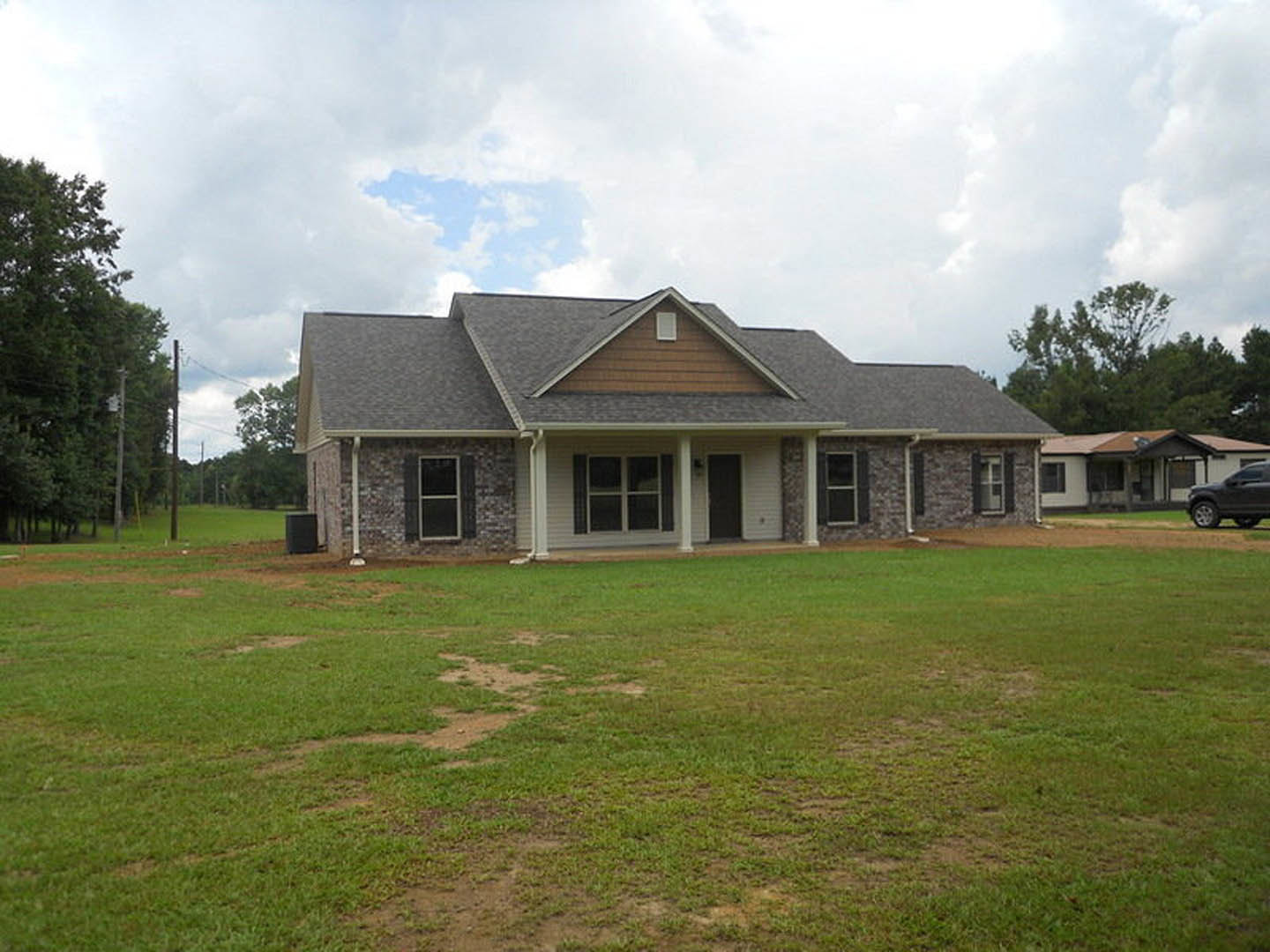 Two-story farmhouse with gray siding, white trim, covered front porch, and large green lawn under partly cloudy sky