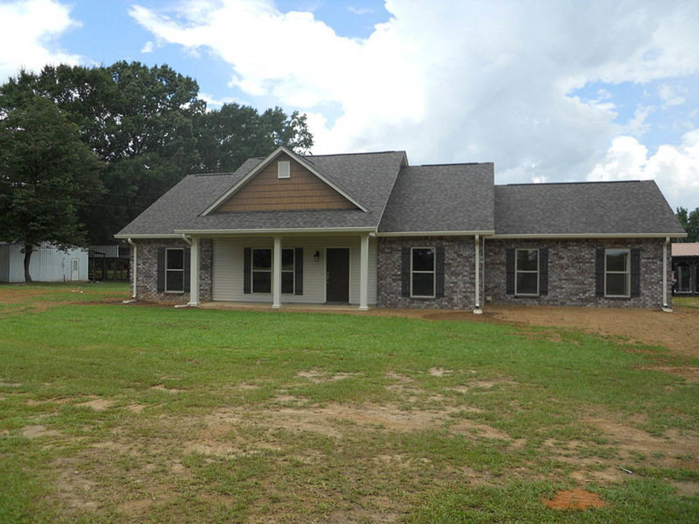 Two-story house with brick and stone exterior, black front door with white trim, white-framed windows, and manicured green lawn in front
