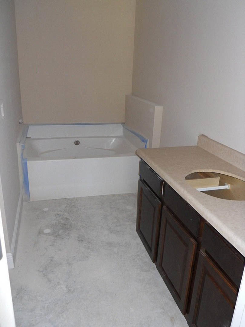 Bathroom featuring a granite countertop with a circular white sink, white tile flooring, freestanding white bathtub with silver faucet, and brown cabinetry.