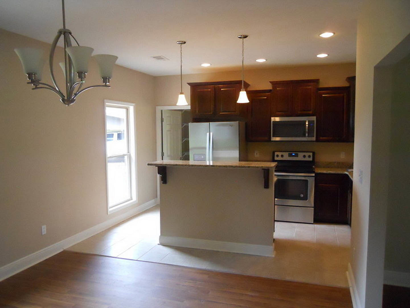 Open-concept kitchen featuring a bar with dark countertops, stainless steel stove, white cabinetry, and a window with a white frame; modern appliances and chandelier visible.