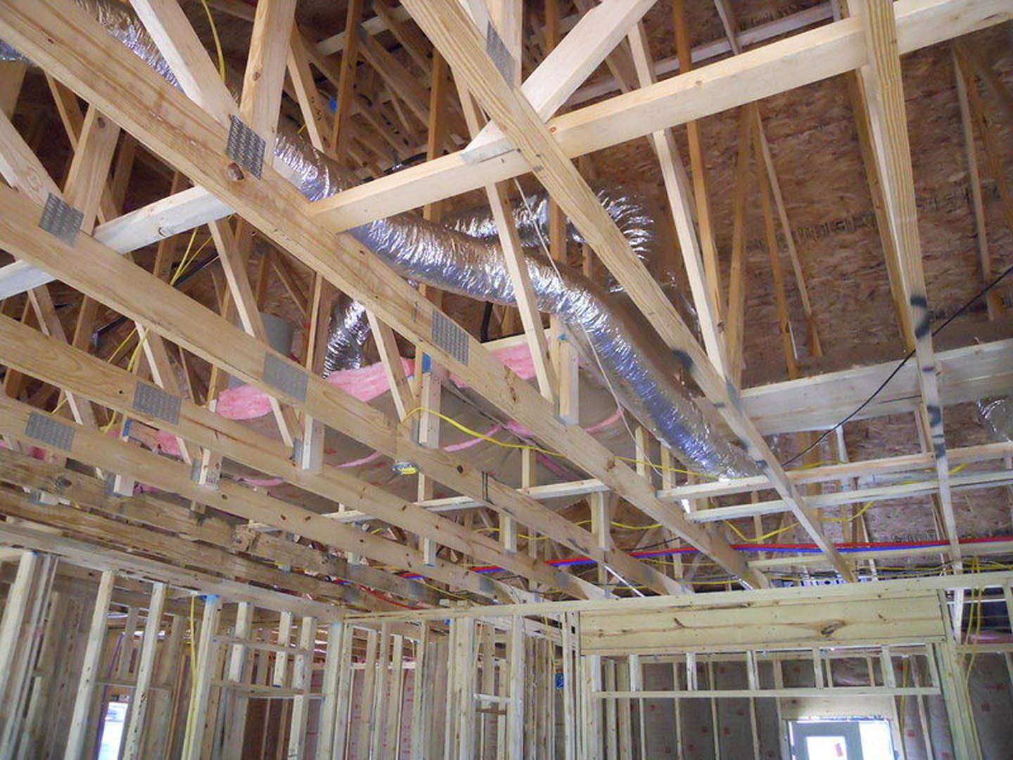 Wood-framed room with exposed silver metal pipes and ceiling beams during construction, insulation visible between planks
