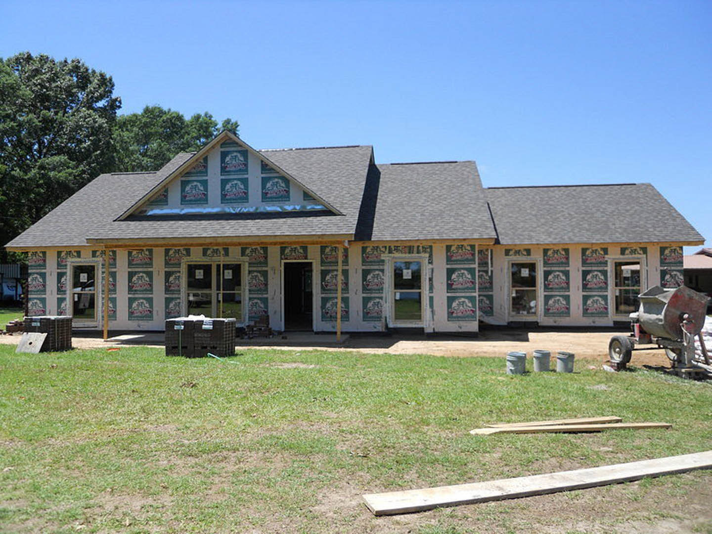 Two-story house with white siding, black-framed windows, and a black front door, surrounded by a green lawn and mature trees under a clear sky.