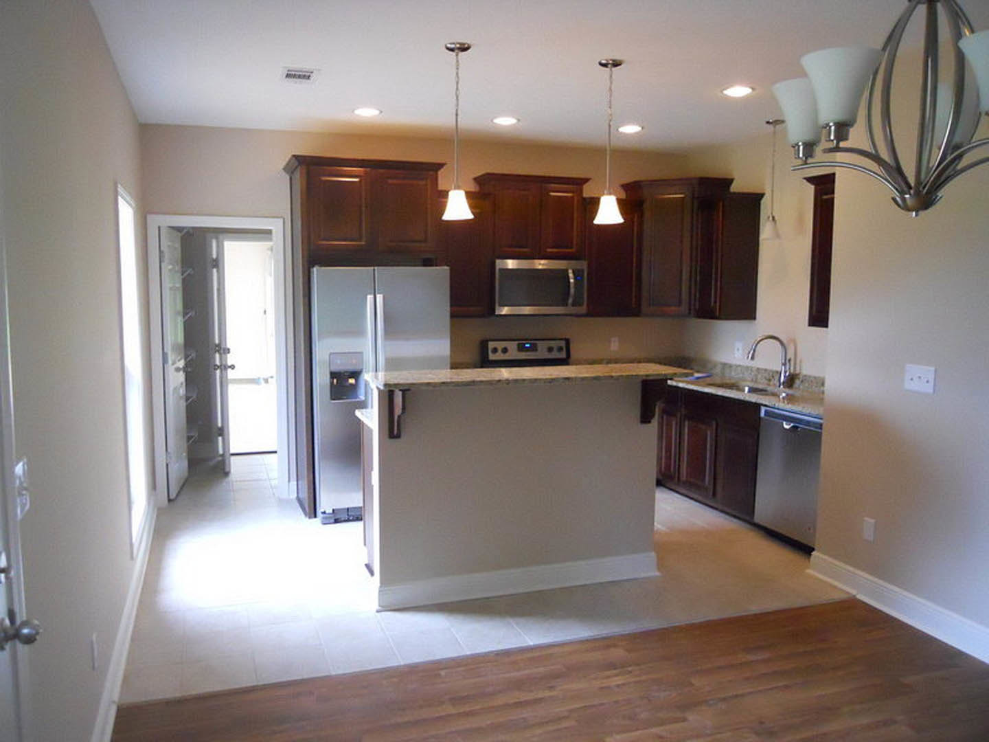 Kitchen with stainless steel refrigerator and stove, white cabinetry, stone countertop, tile backsplash, and hardwood flooring