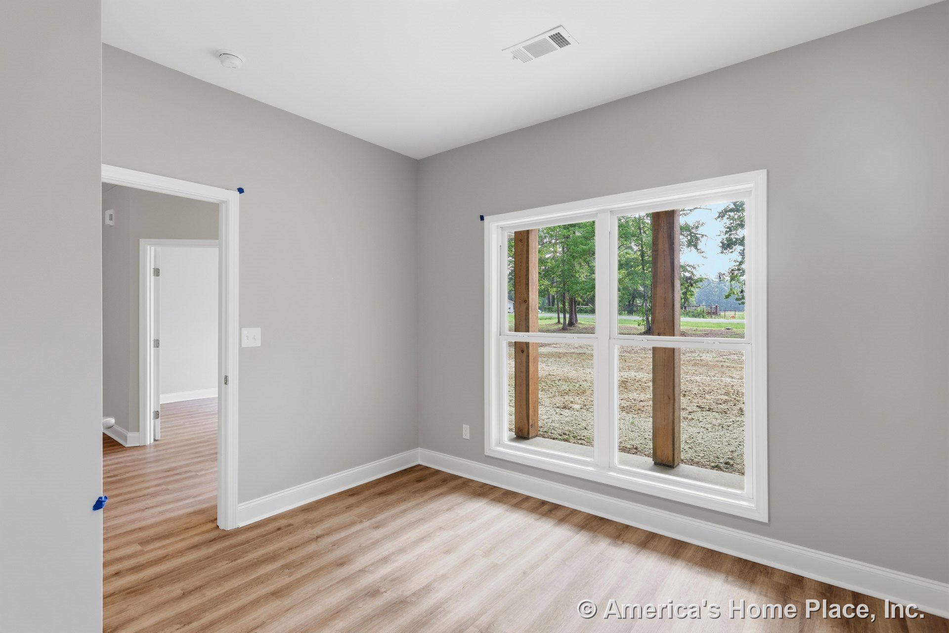 Large double windows with white trim allow natural light into a room with light wood plank flooring, gray painted walls, white baseboards, an open doorway, and a ceiling vent.