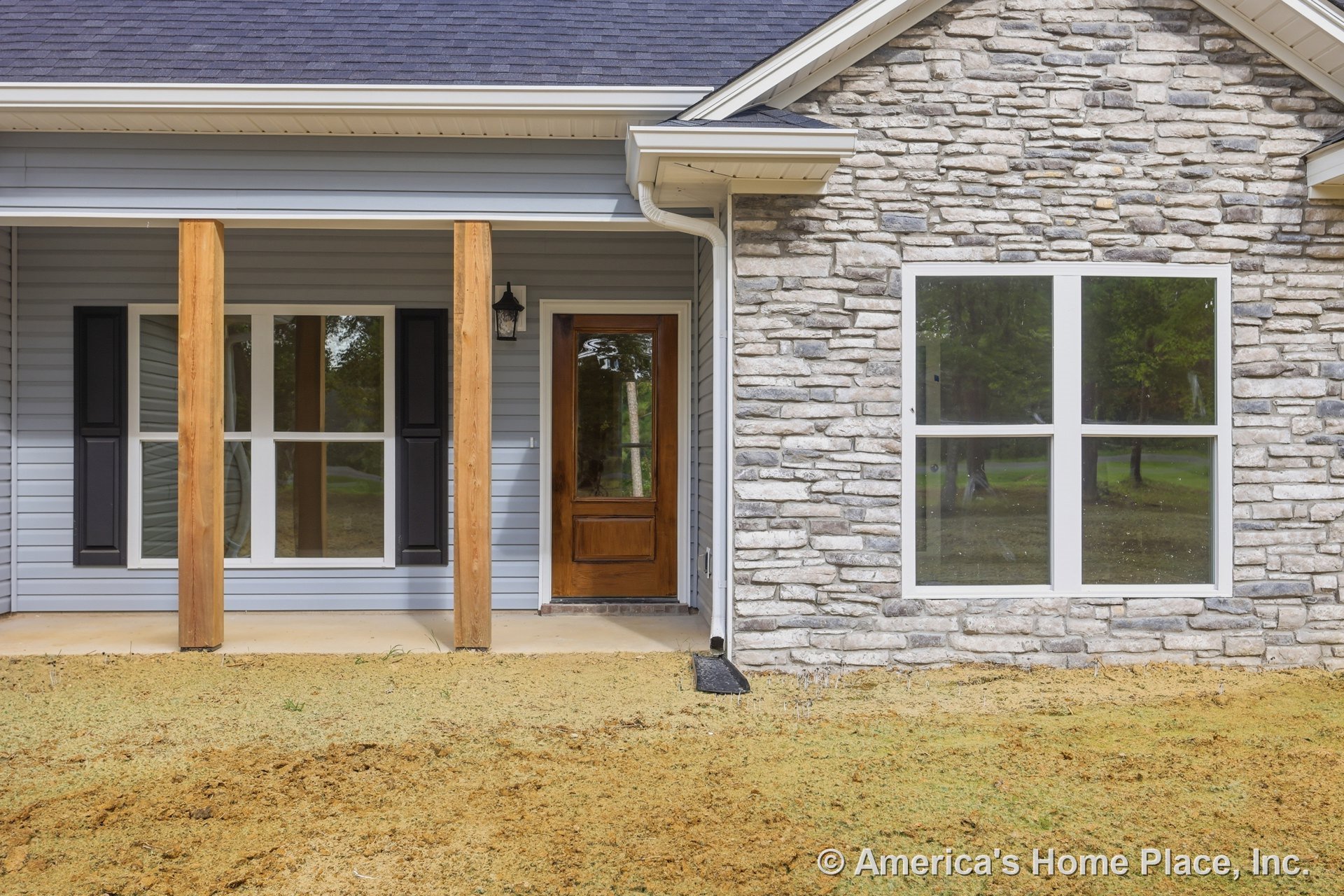 Stone veneer and horizontal siding exterior with covered front porch supported by wooden columns, large windows, wood front door, decorative trim, roof overhang, and porch lighting