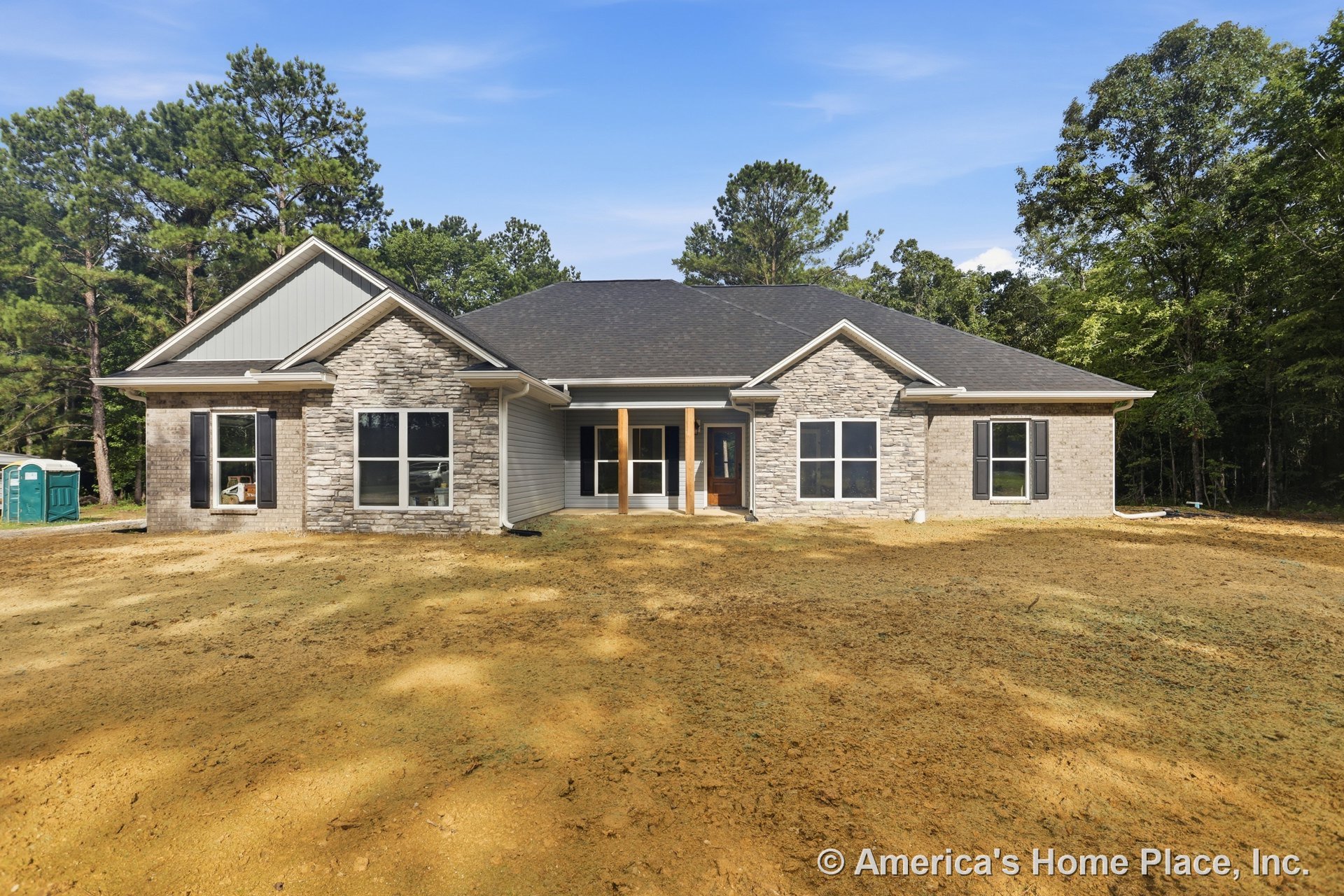 Stone veneer and brick siding exterior with covered entry porch, double front windows, dark shingle roof, wood porch columns, and detailed trim around the front door.